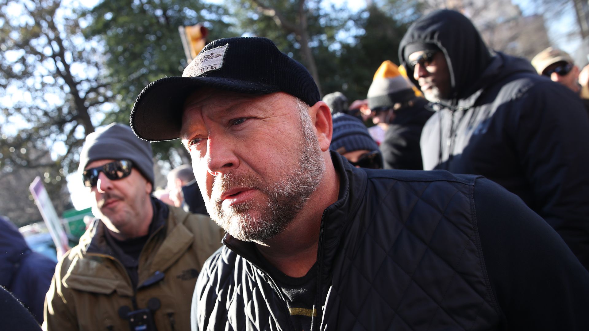 Photo of Alex Jones in a cap surrounded by protesters