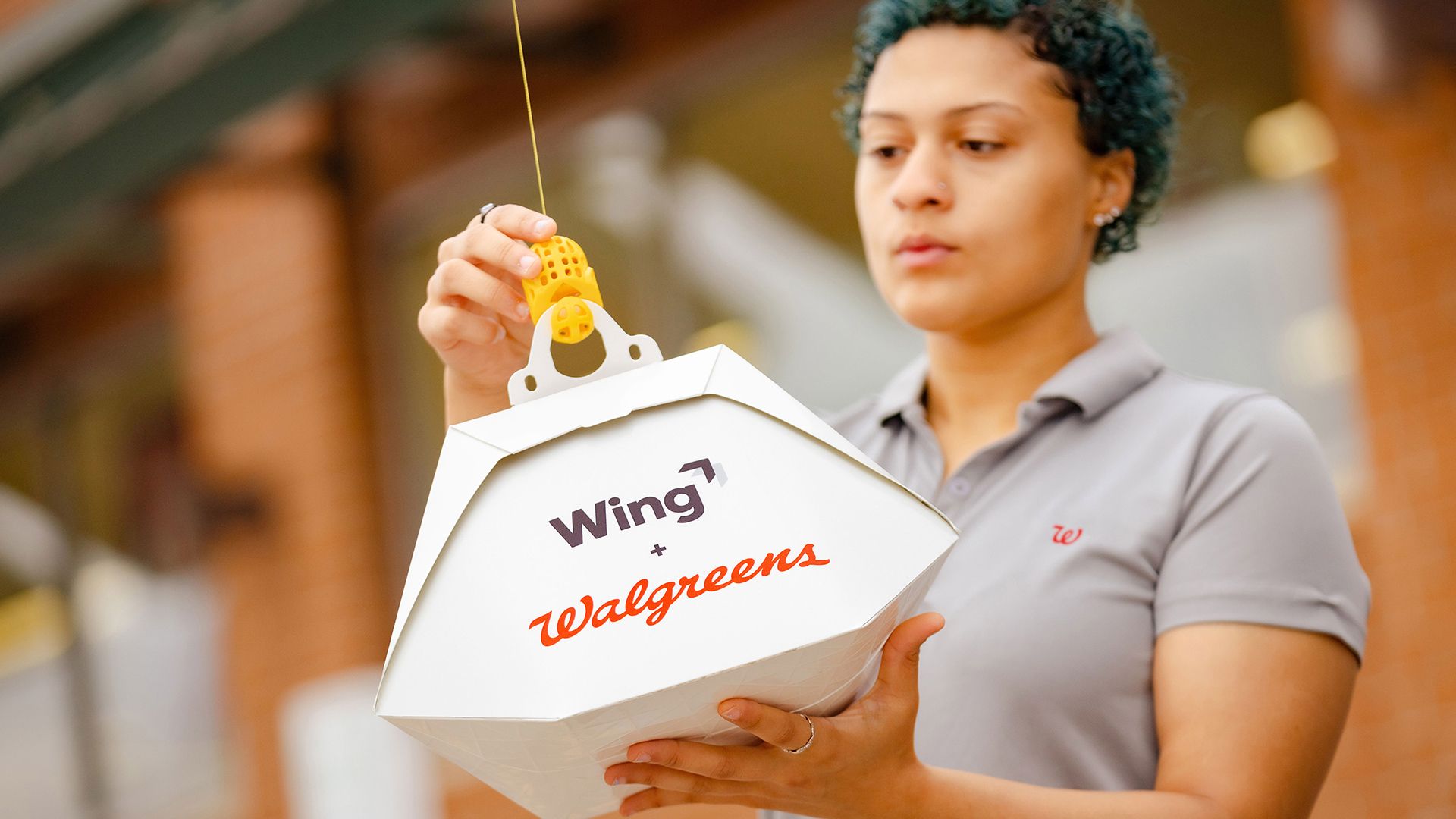 Image of a Walgreens employee clipping a customer order to a Wing drone tether