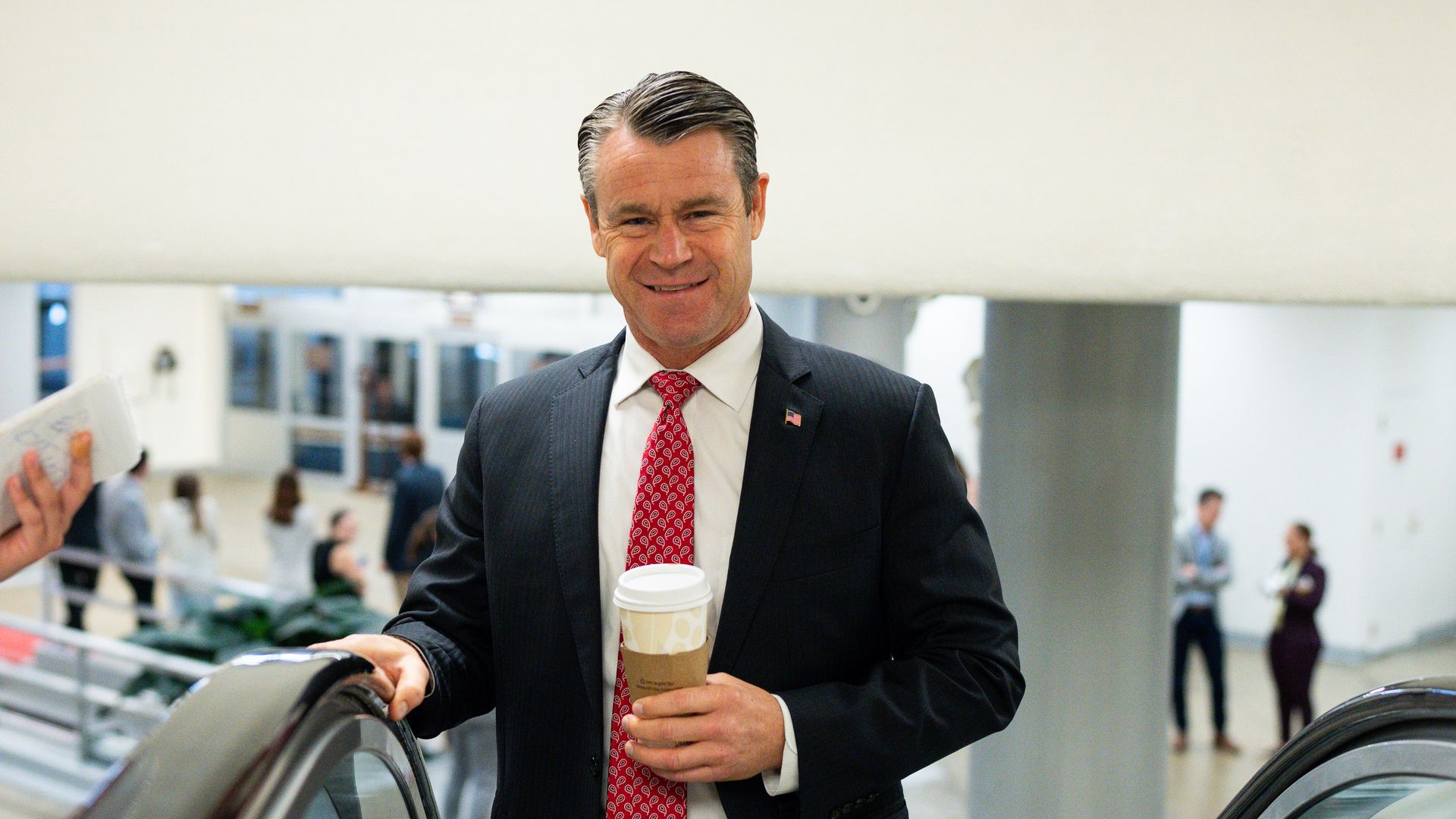 A man holding a coffee on an escalator