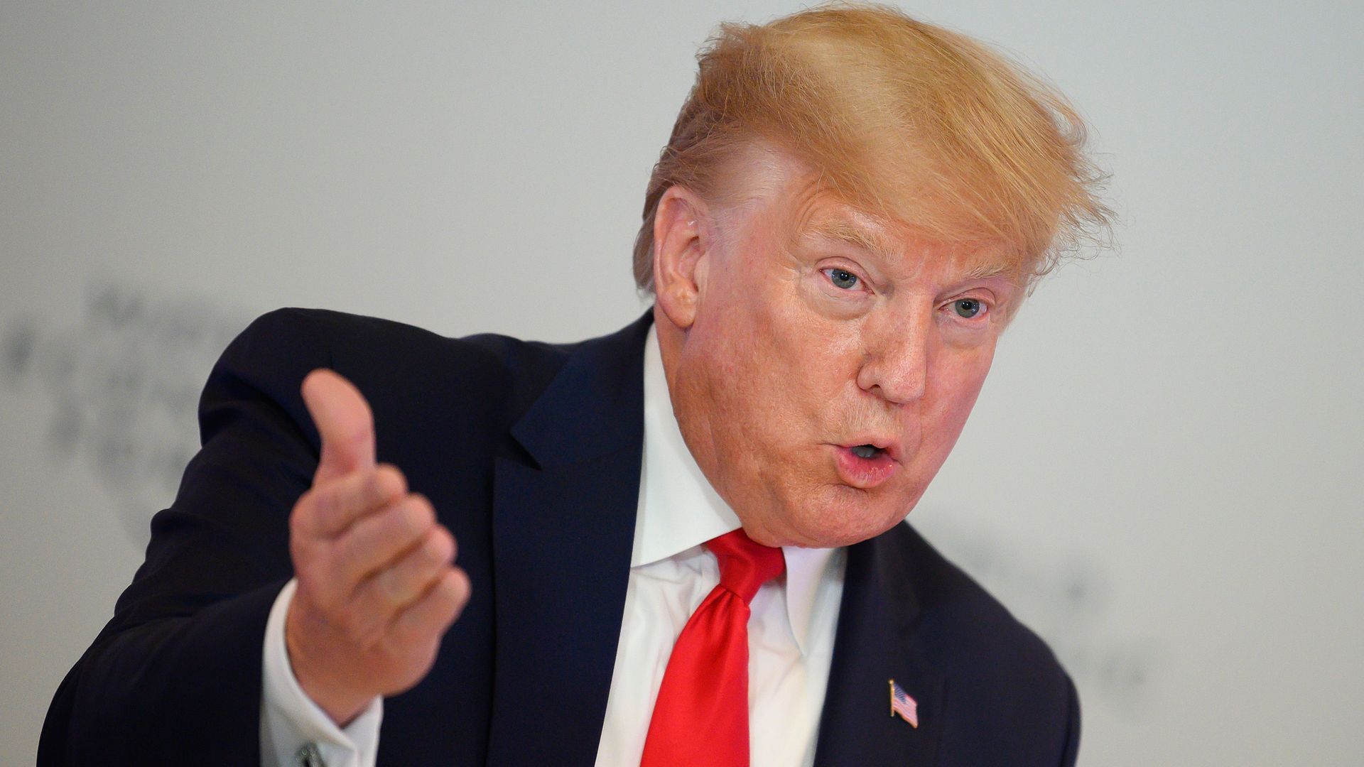 In this image, President Trump stands and wears a suit and tie and talks