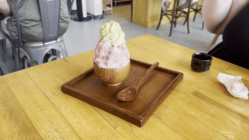 A hand scoops a bite out of a pink snoball with green whipped cream on top. 
