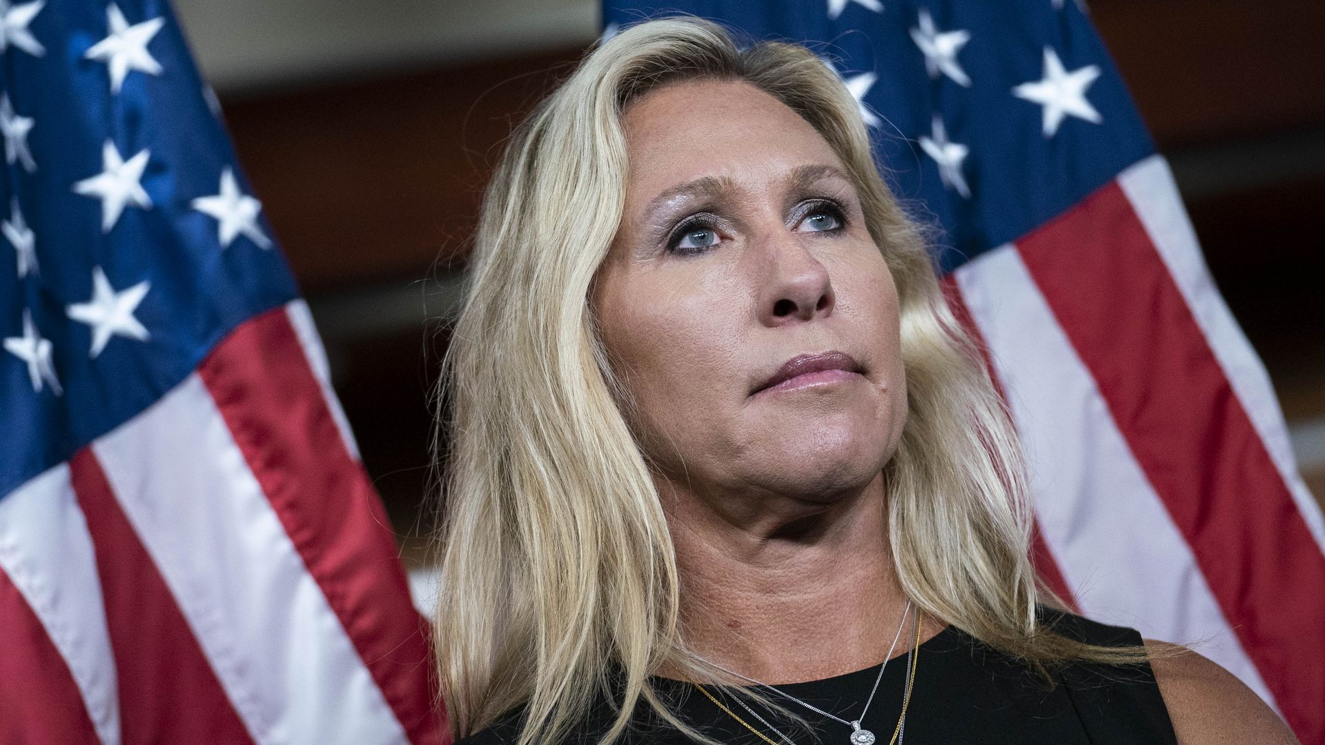 Rep. Marjorie Taylor Greene is seen standing in front of an American flag.
