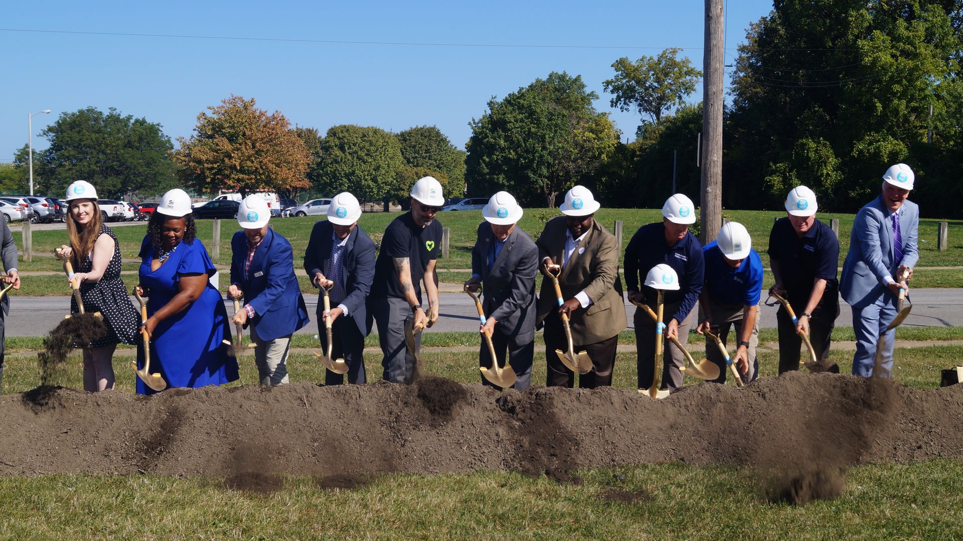 Officials in white hard hats ceremonially break ground with shovels