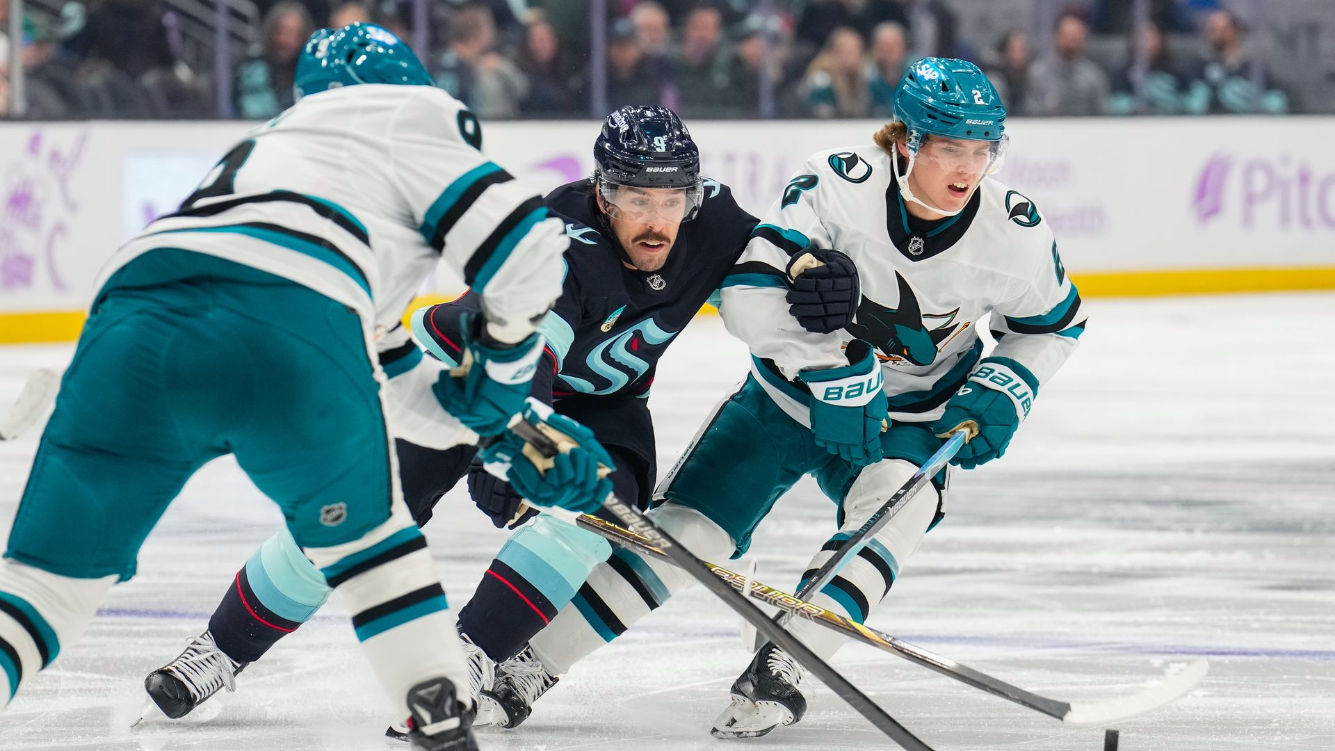 Three hockey players skate fiercely to control the puck. 
