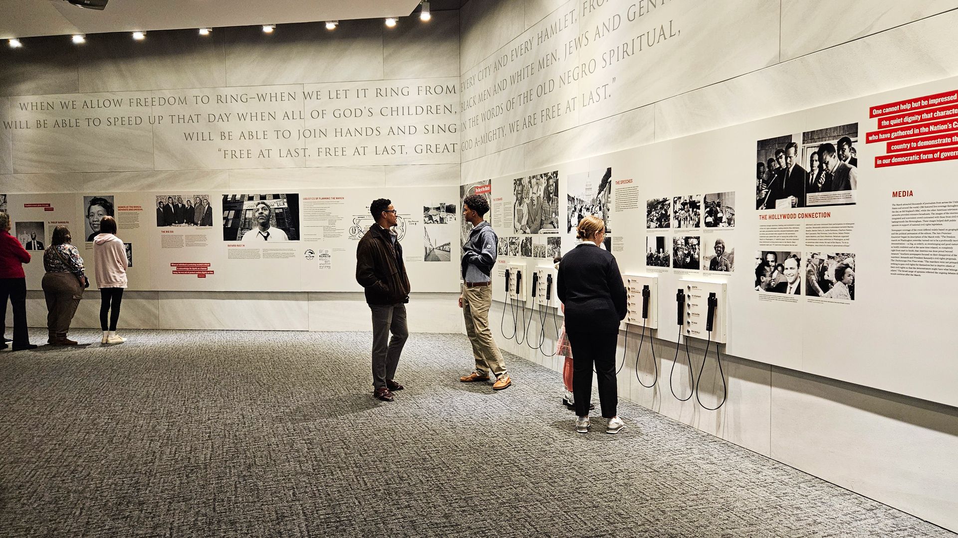 People inside a museum exhibit with large wall text quoting, "Free at last, free at last," and panels featuring historic photos, text, and listening devices about civil rights.