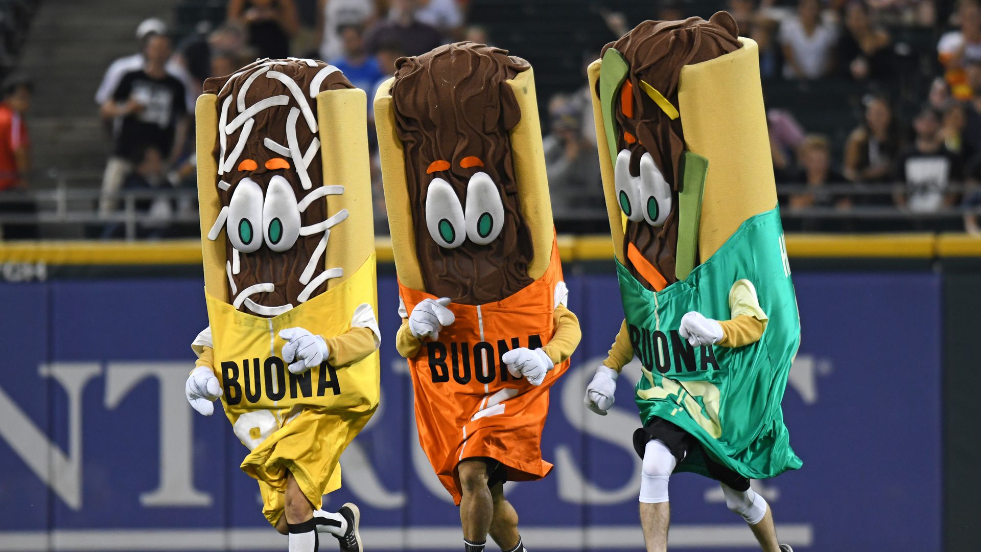 Photo of three mascots dressed up like sandwiches at a baseball game. 