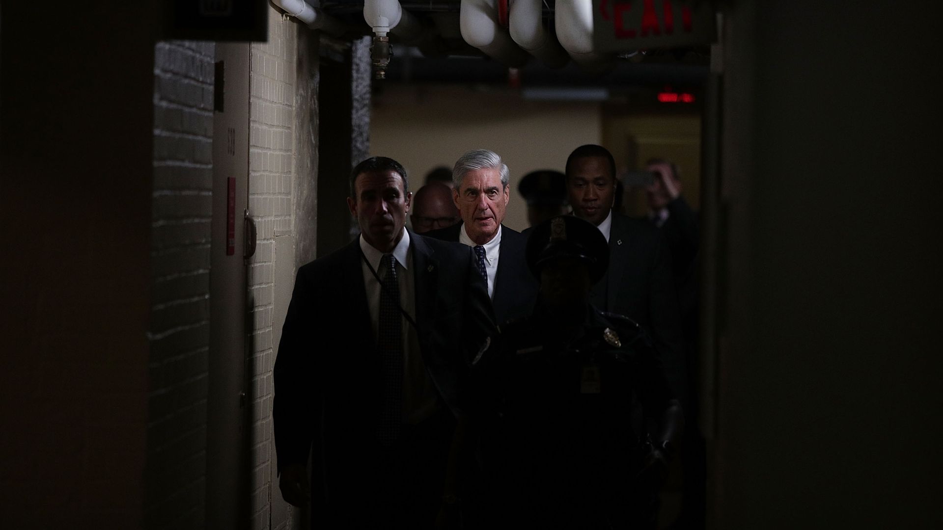 Robert Mueller is illuminated as he walks down a hallway at the Capital surrounded by security guards