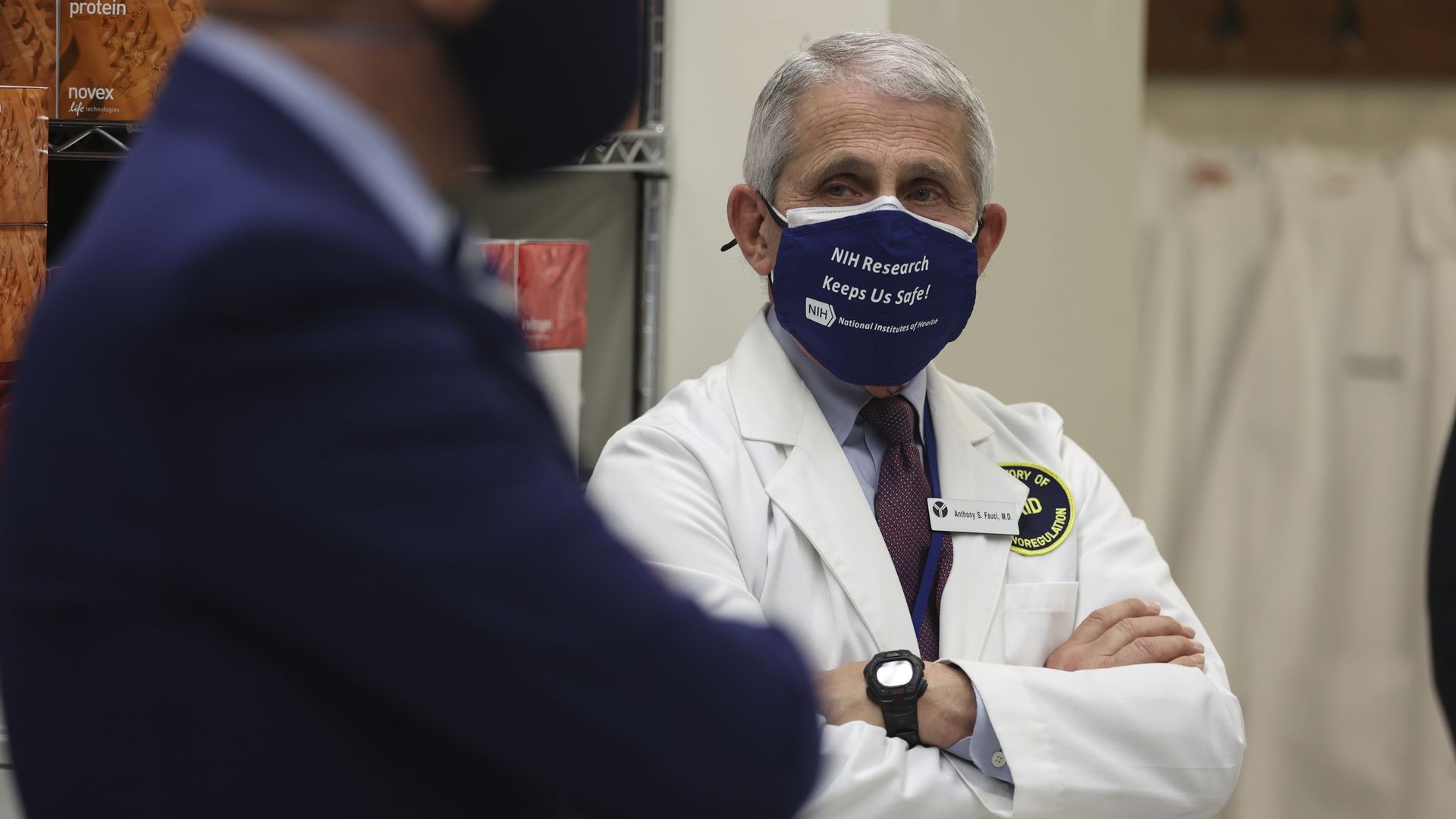 Dr. Fauci wears a mask and lab coat
