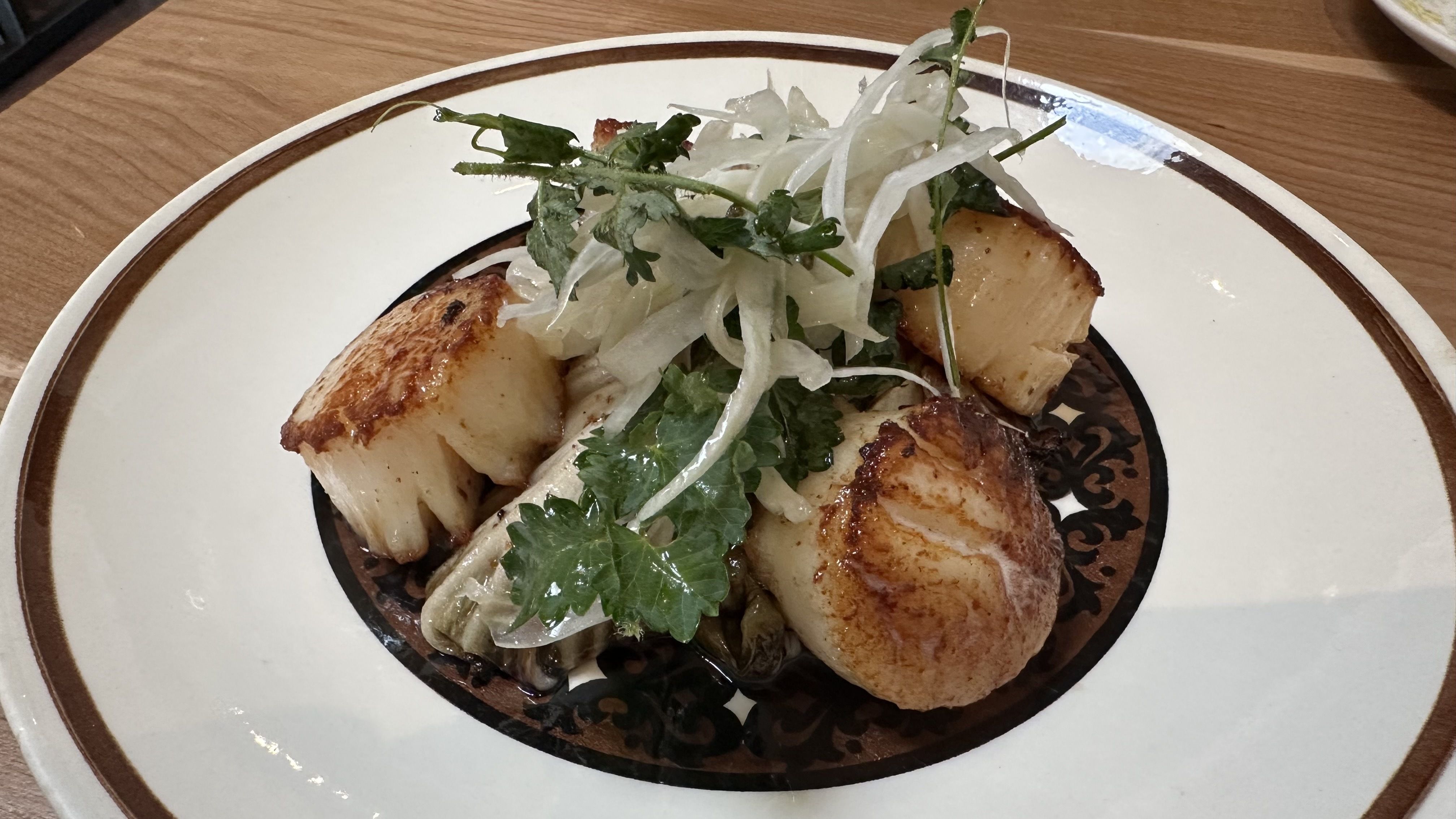 Seared scallops with grilled radicchio and shaved fennel and herbs on a plate.