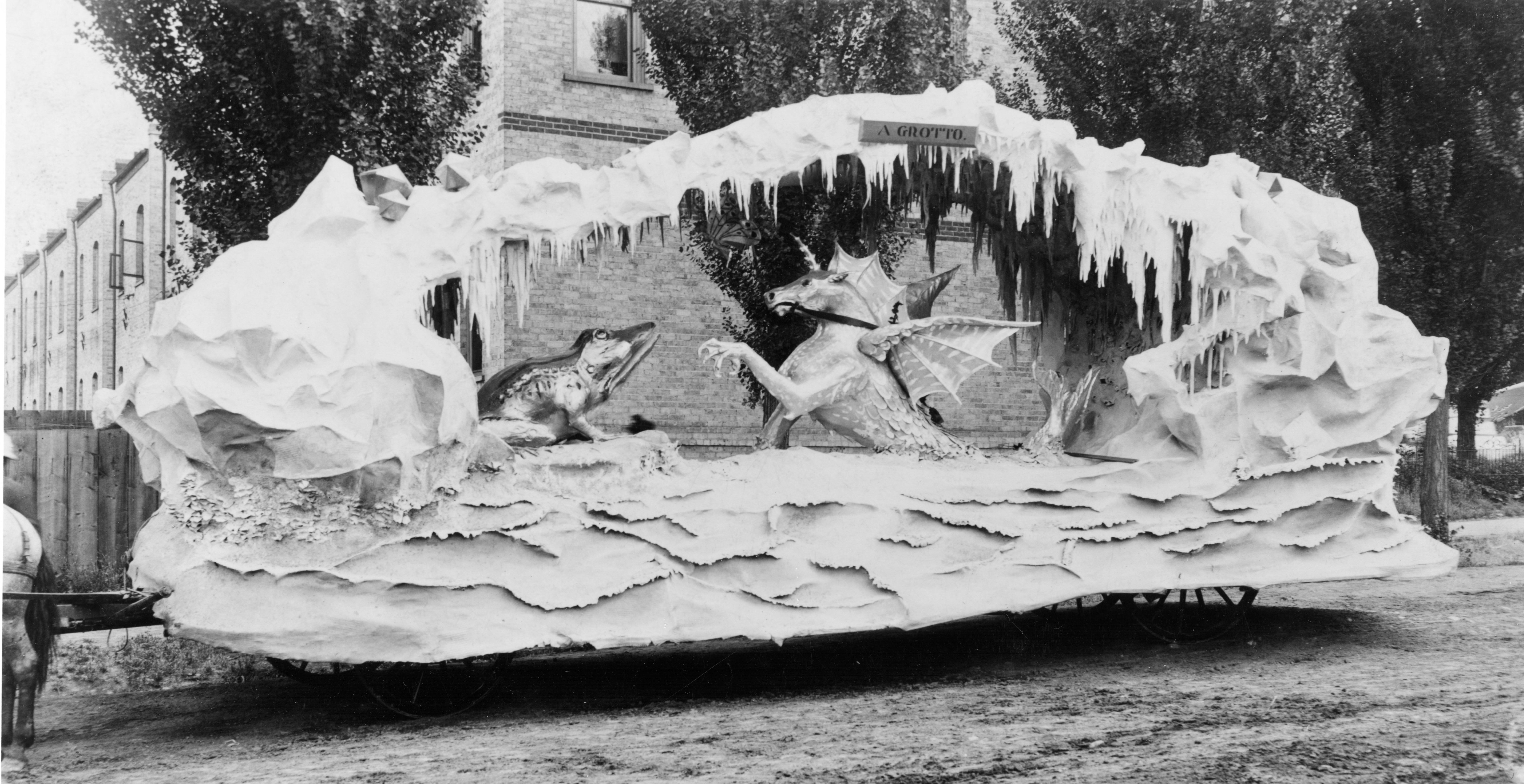 An 1897 parade float features a frog being attacked by an alicorn-dragon in an ice cave.