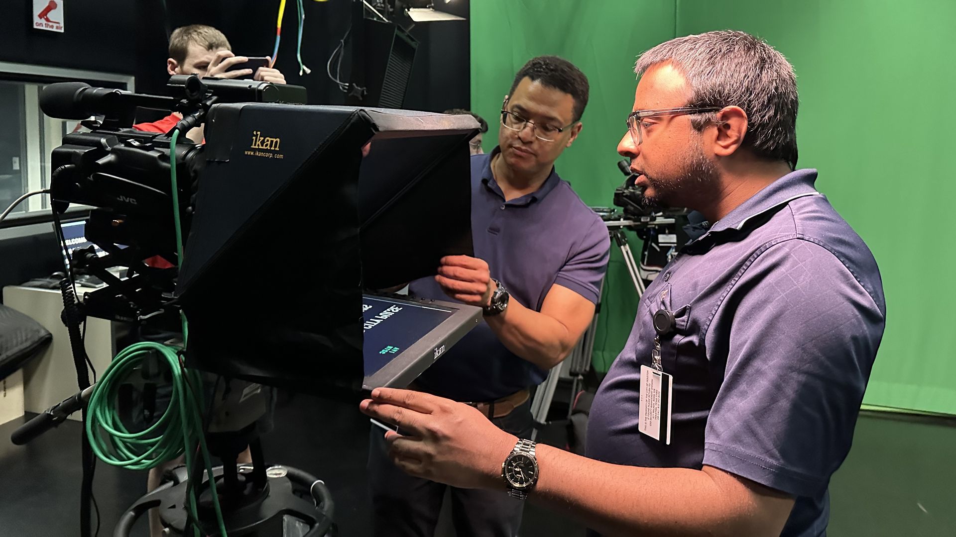 Two people examine a teleprompter inside a TV studio