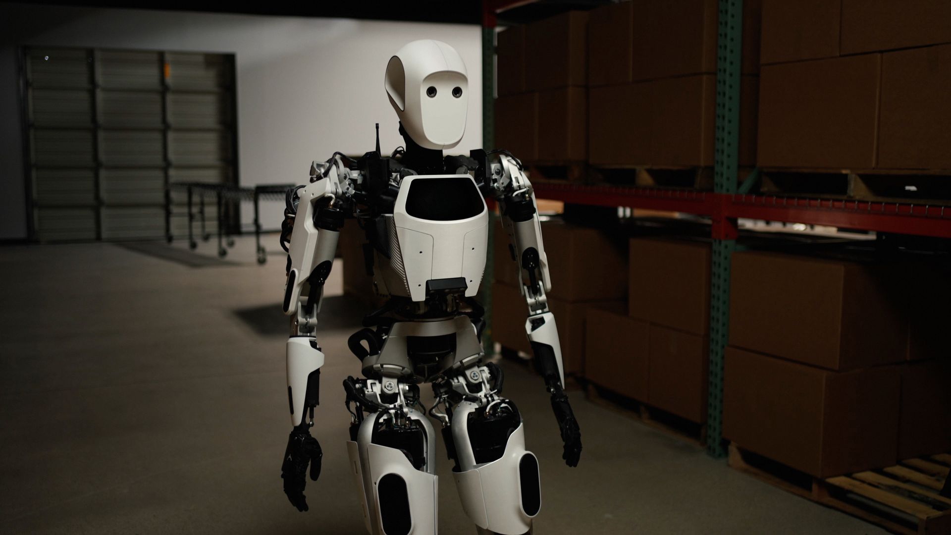 A humanoid robot walks through an office /warehouse space.