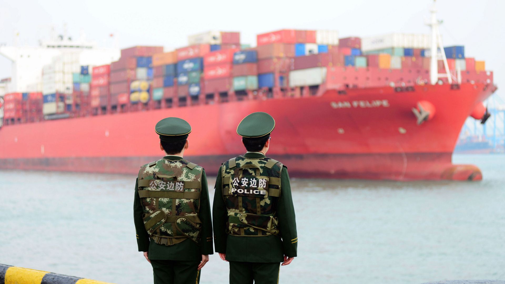 Two Chinese policemen look at the harbor where they wait for a large containership arrive