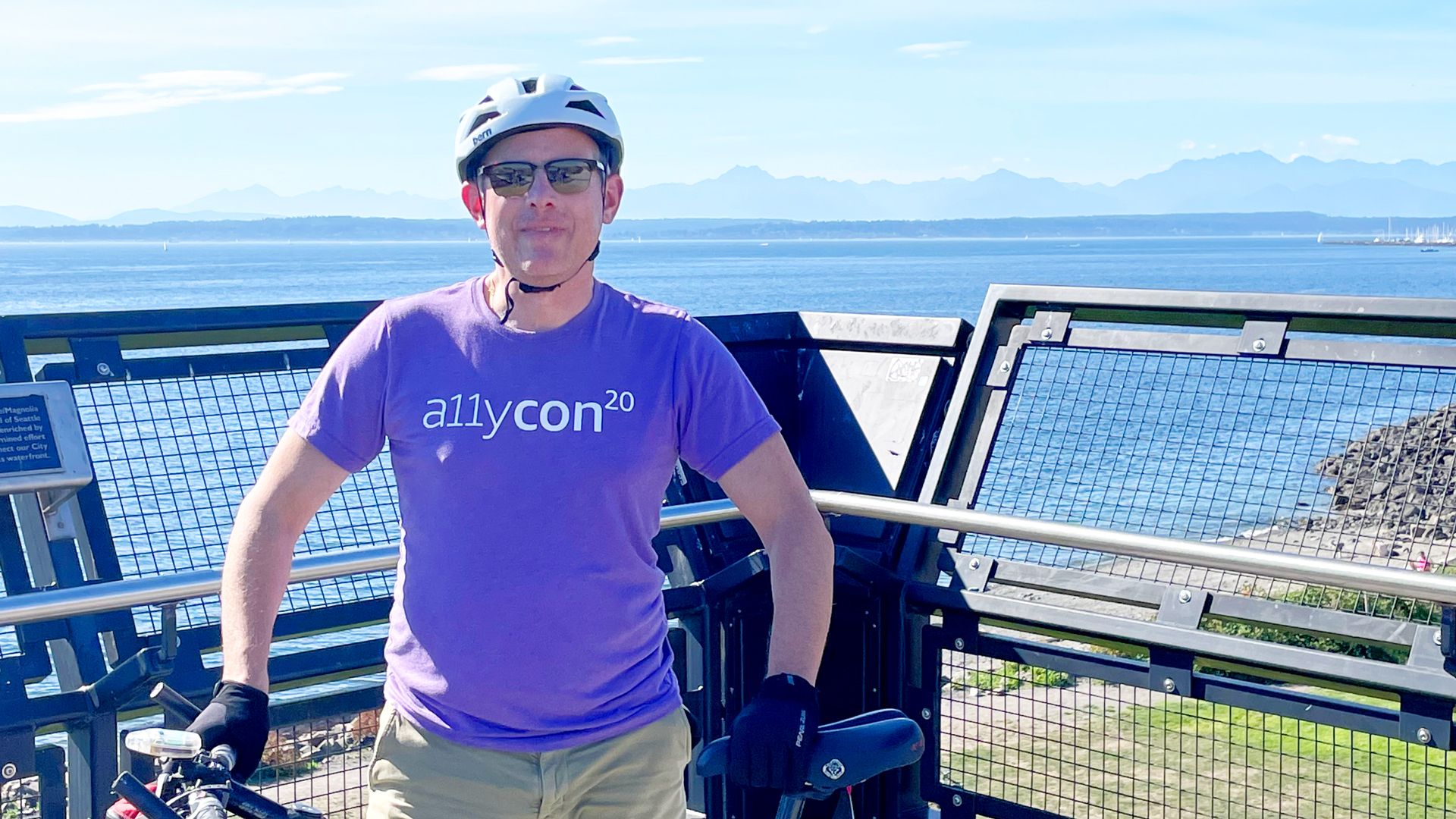 A man in a purple shirt and a bike helmet at a scenic overlook somewhere near Seattle. 