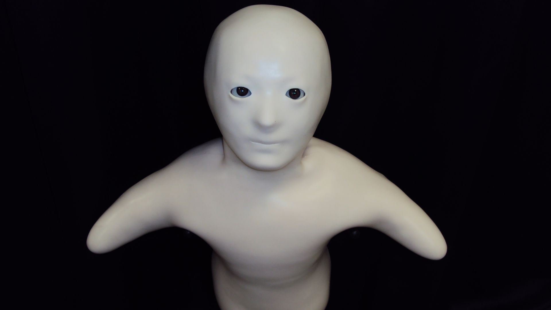 A white, baby-like robot with stumps for arms on a dark background
