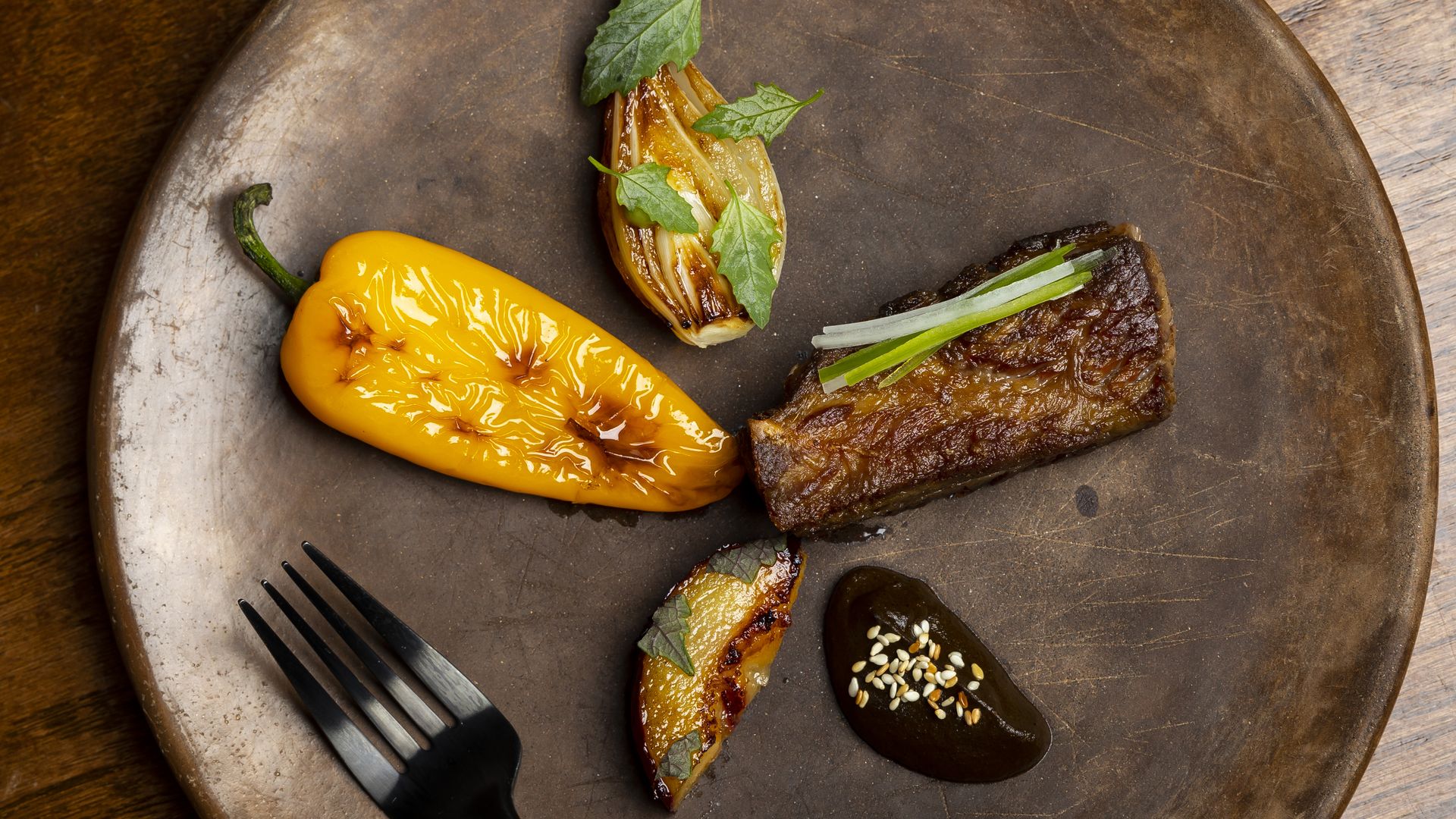 Photo of a Carne Asada plate featuring a 73hr barbacoa-spiced short rib, cebolla, chile tatemado, local stone fruit and eggplant puree 