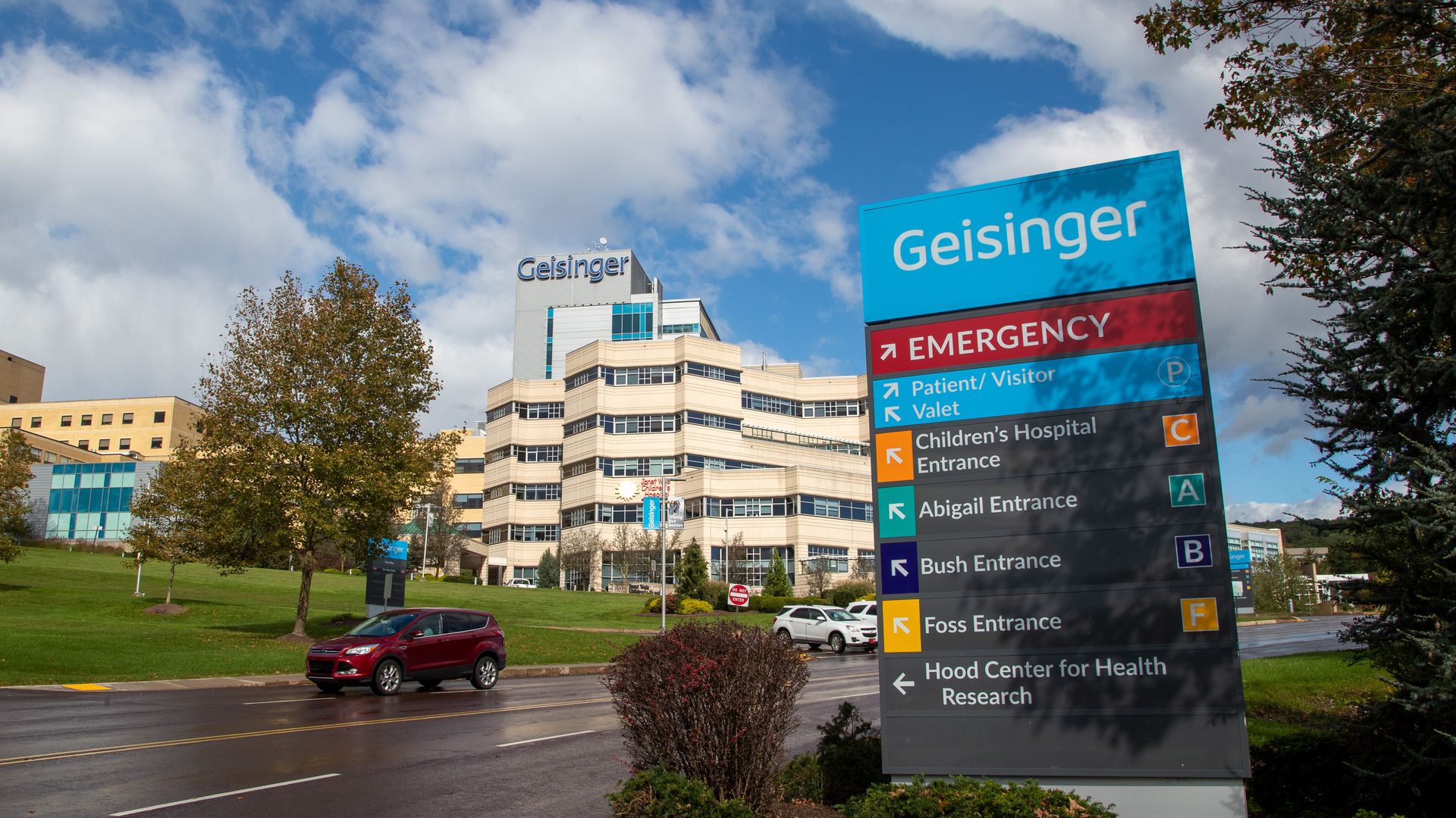 A picture of the sign outside Geisinger Health System with the hospital in the background.