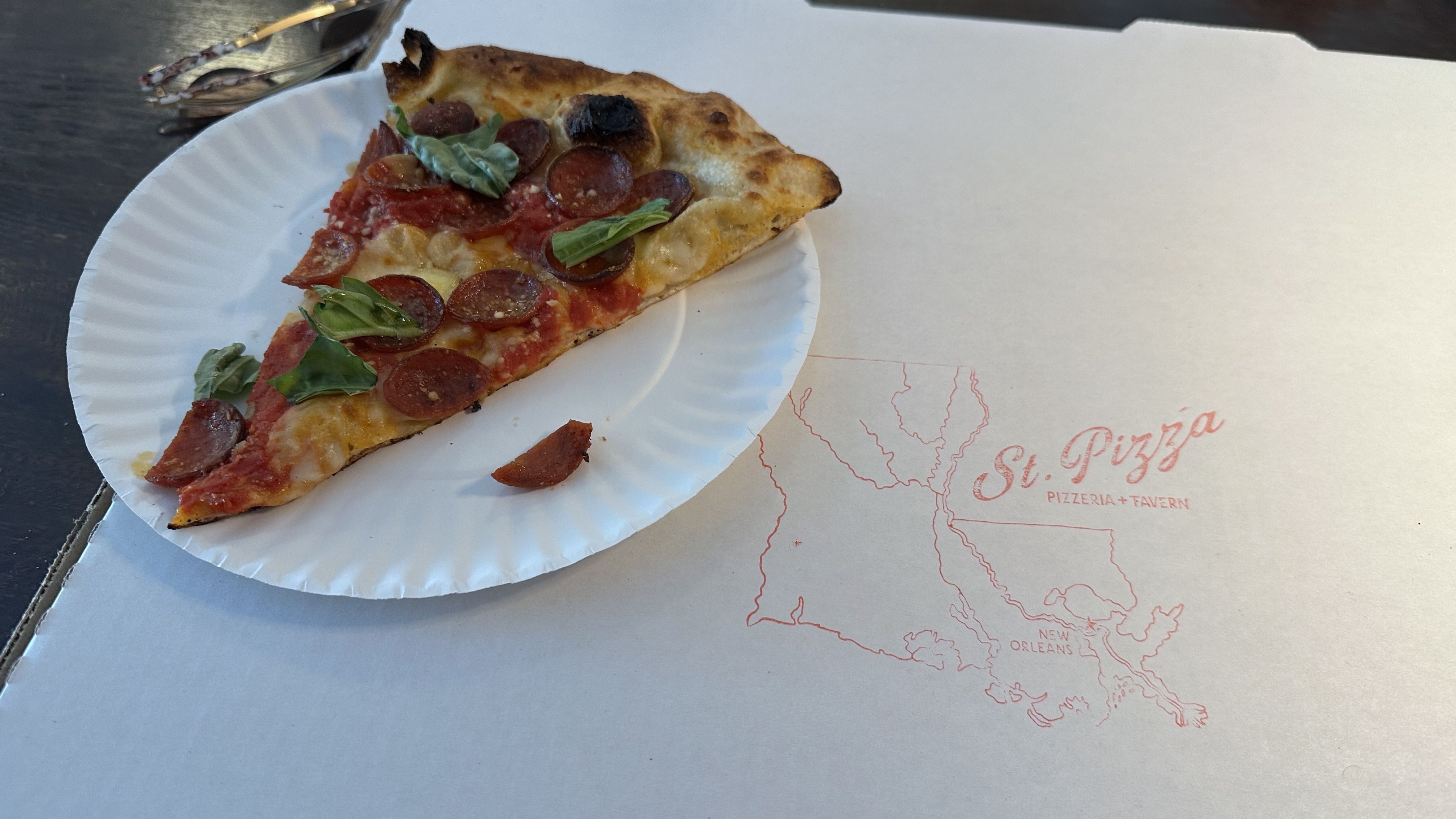 A slice of pepperoni pizza sits on top of a pizza box with the St. Pizza logo.