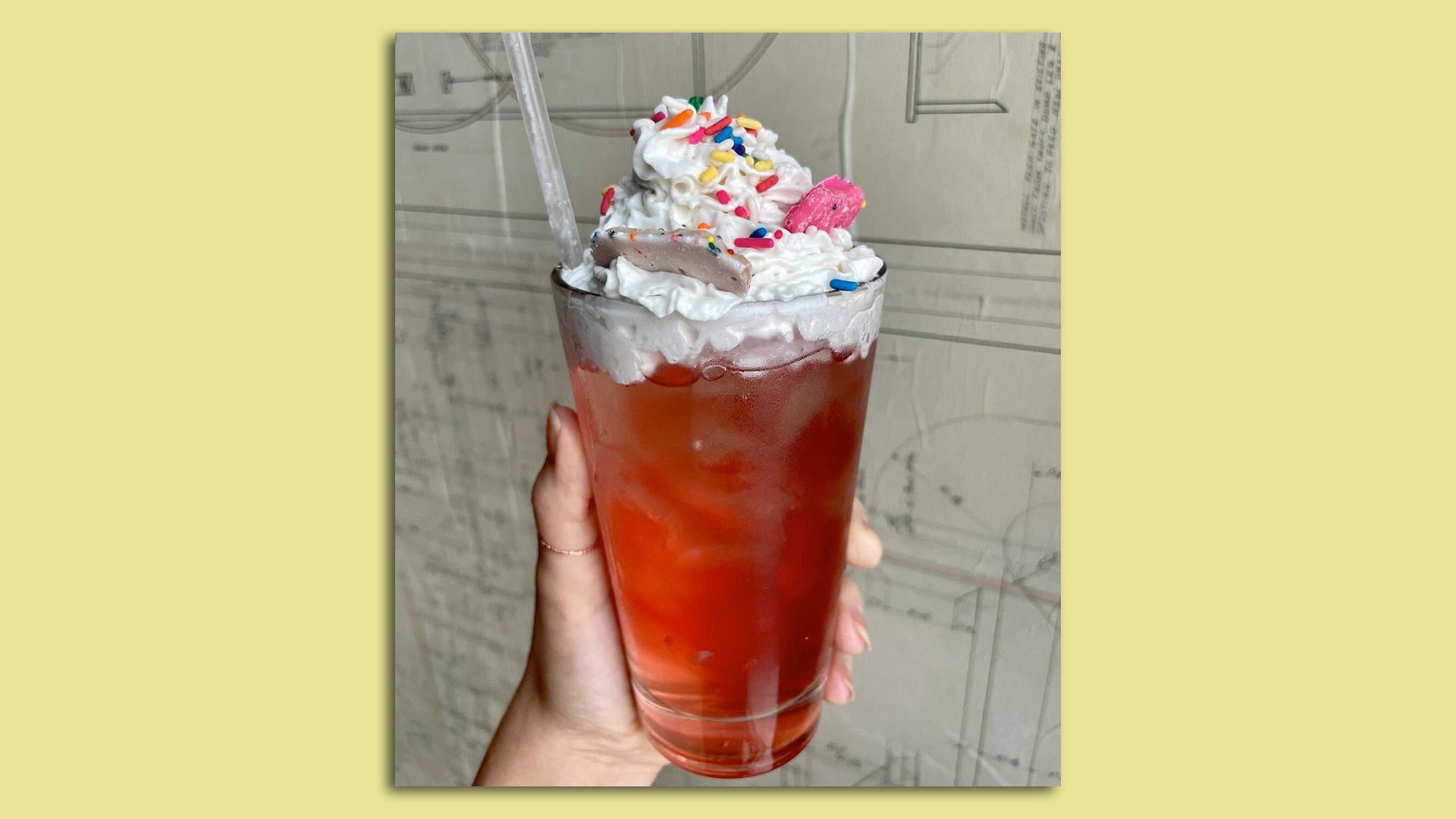 A hand holds up a red cocktail topped with whipped cream and animal crackers.