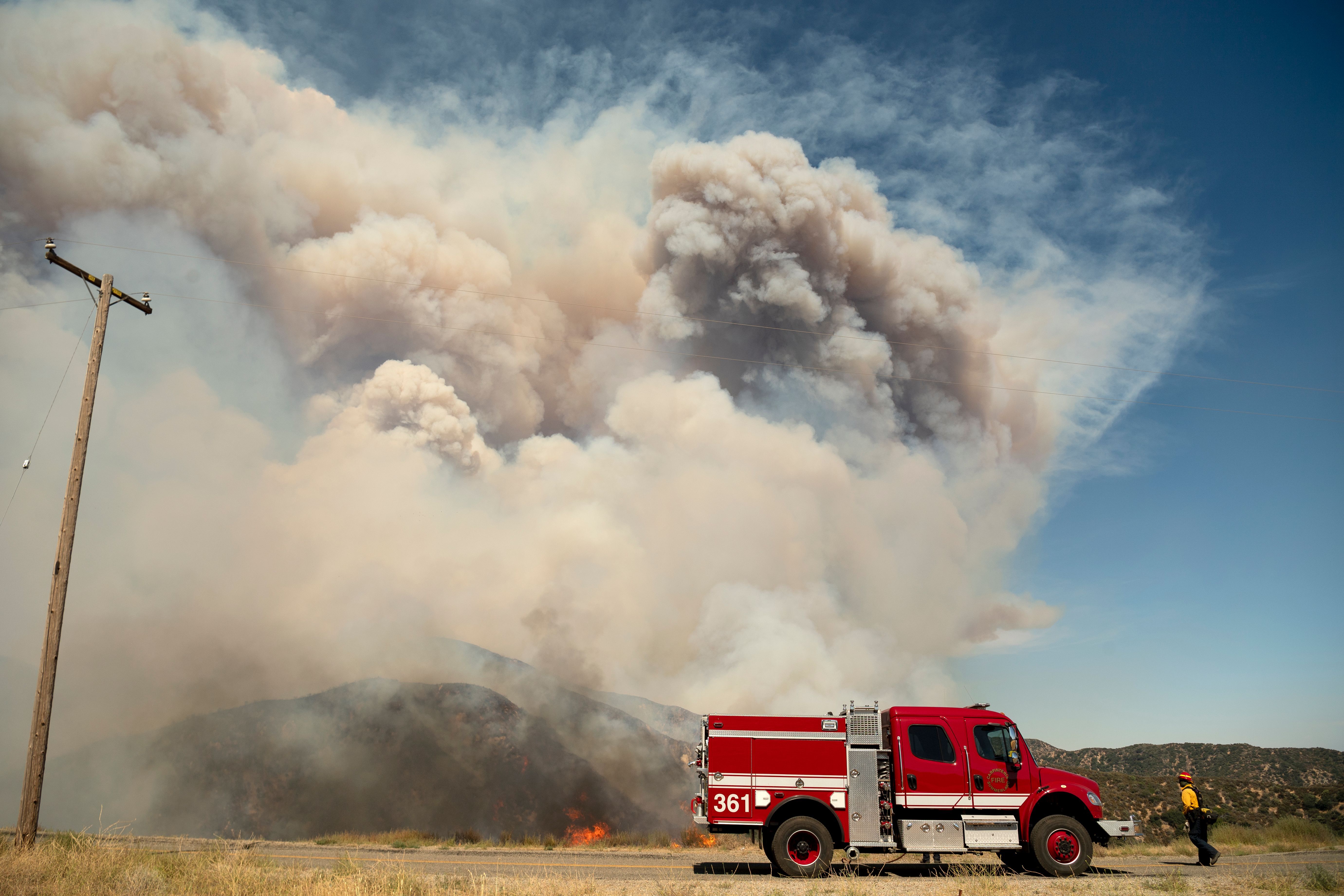 A firefighter walks back to his truck near a pyrocumulus ash plume during the Apple fire near Banning, California on August 1
