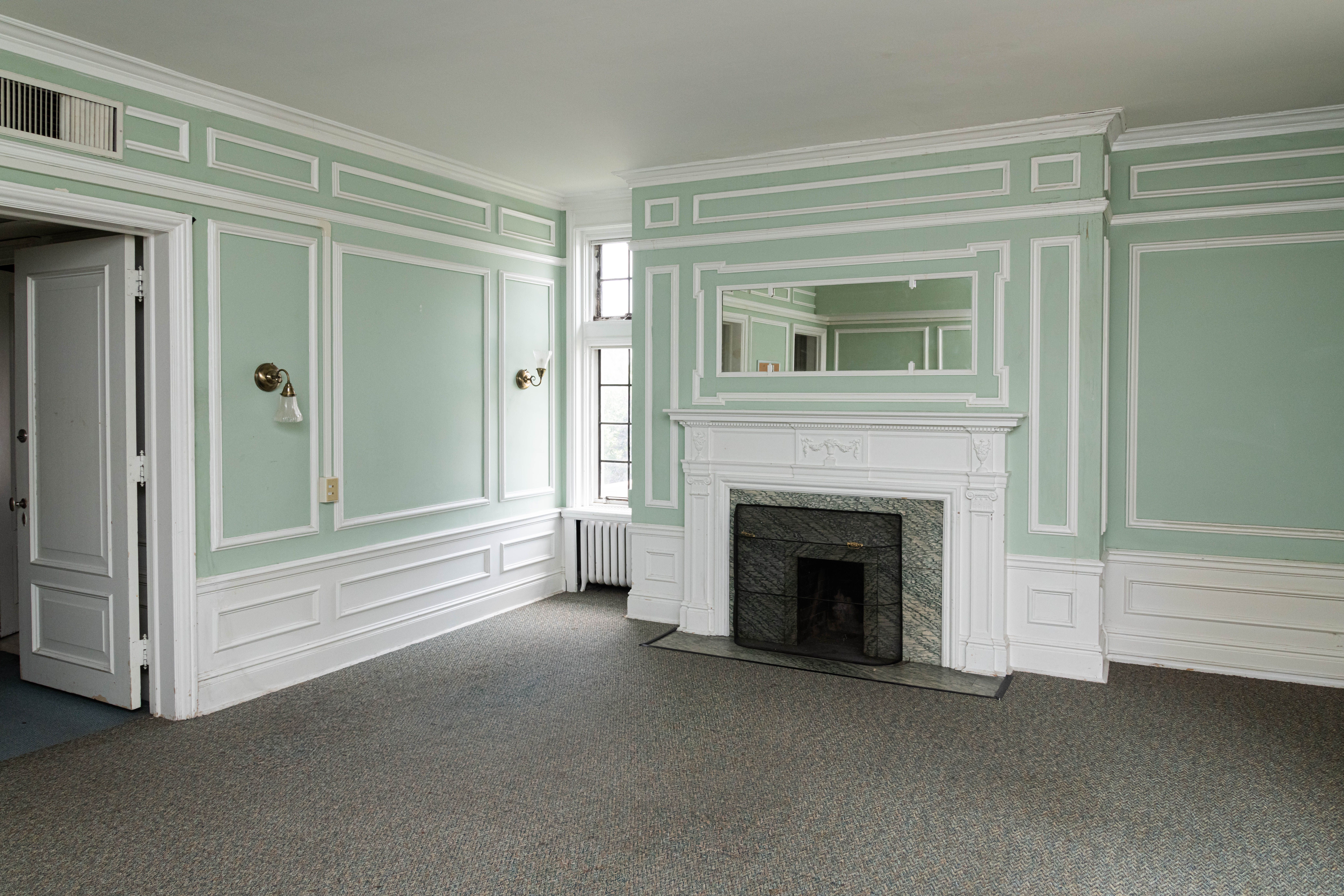 A bedroom with green walls, a fireplace and white accents.