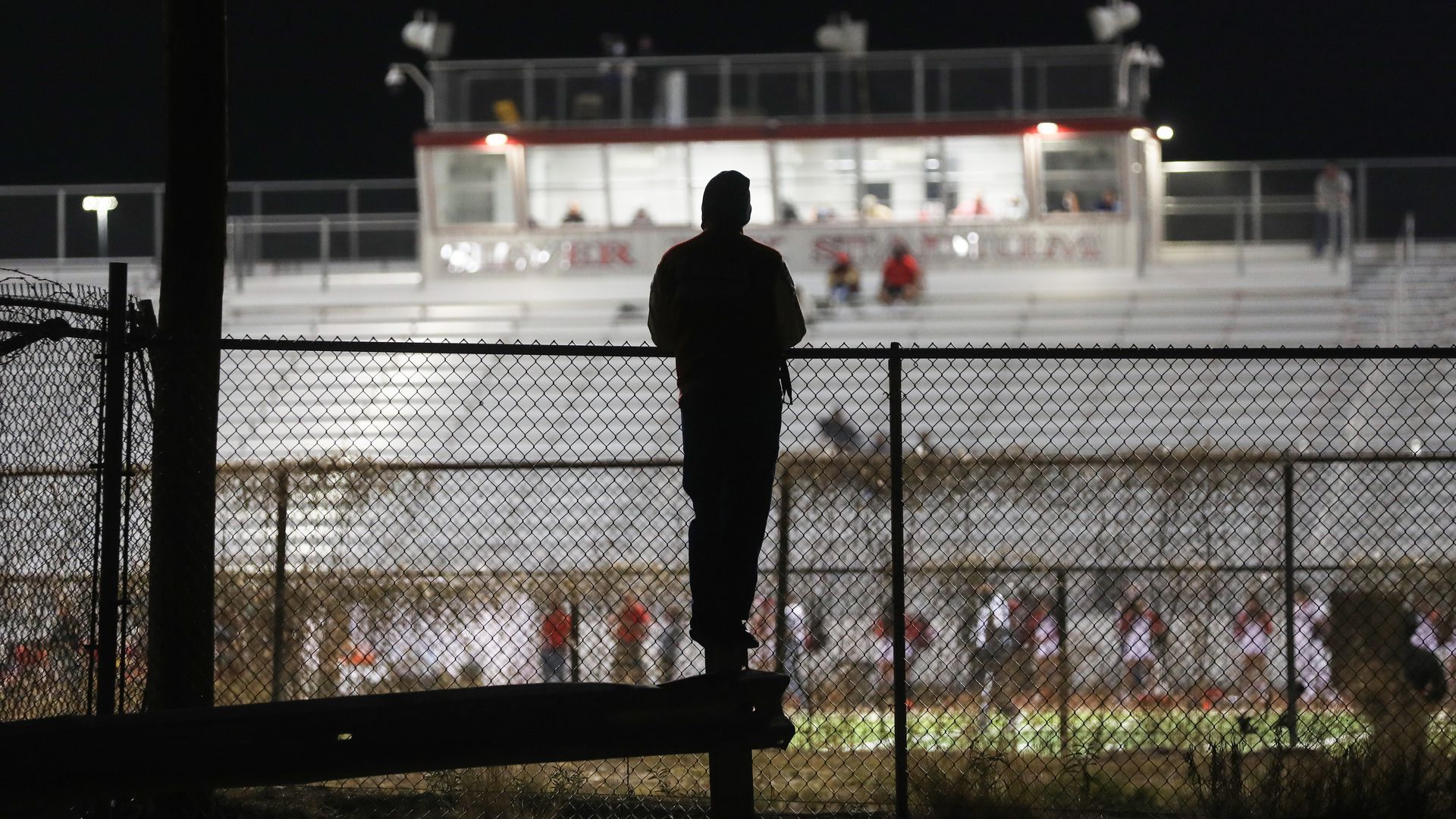 Picture of a person standing behind a fence looking into a football field