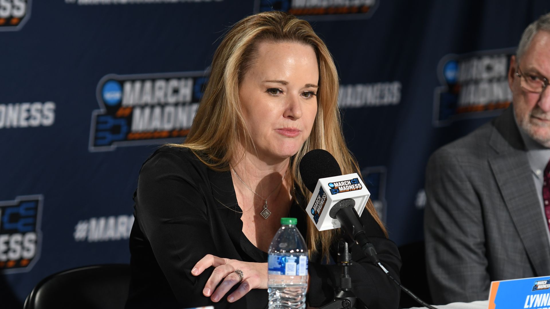 A blonde woman at a microphone during a March Madness news conference.