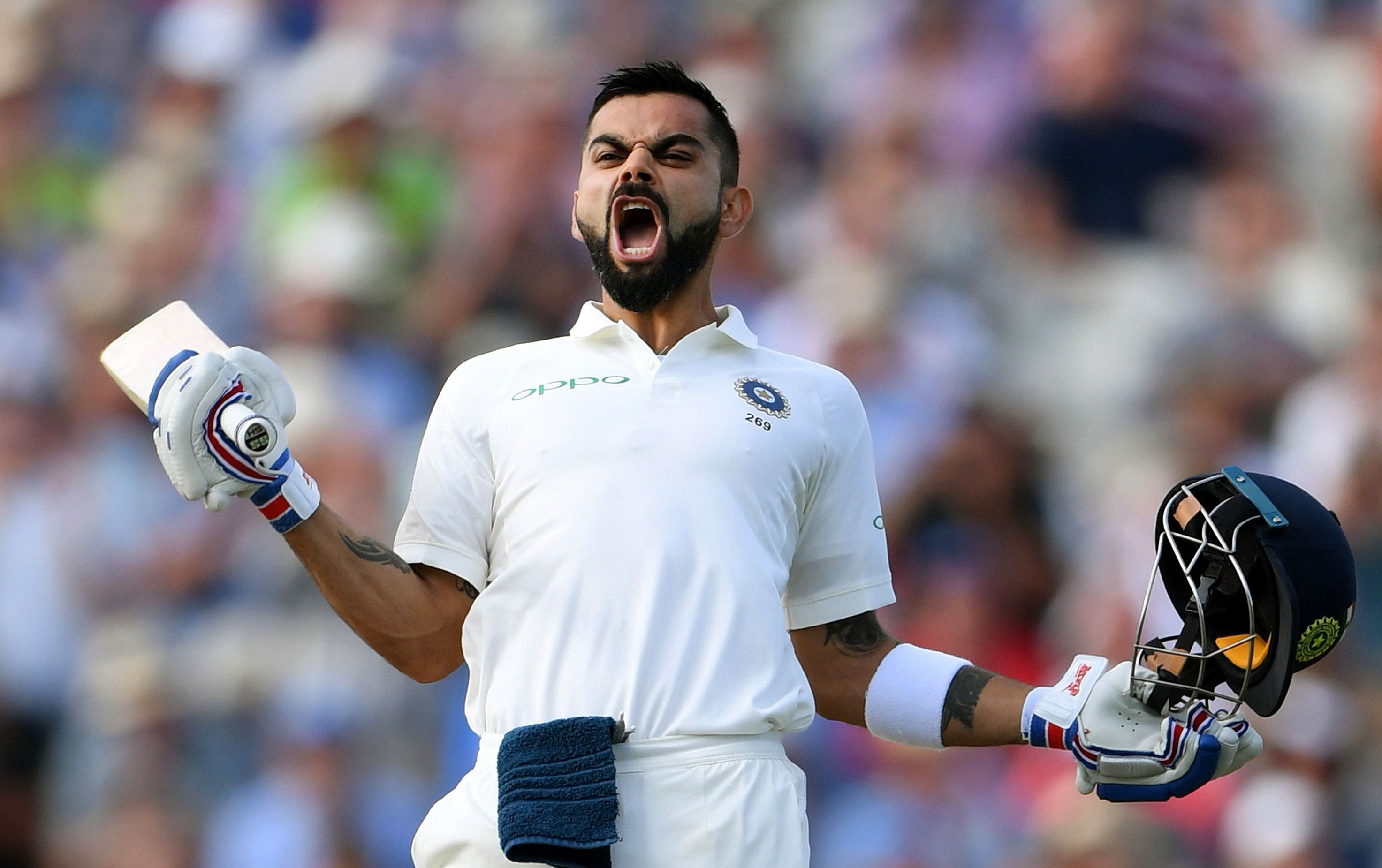 Virat Kohli screaming in triumph while in uniform and holding a cricket bat and helmet