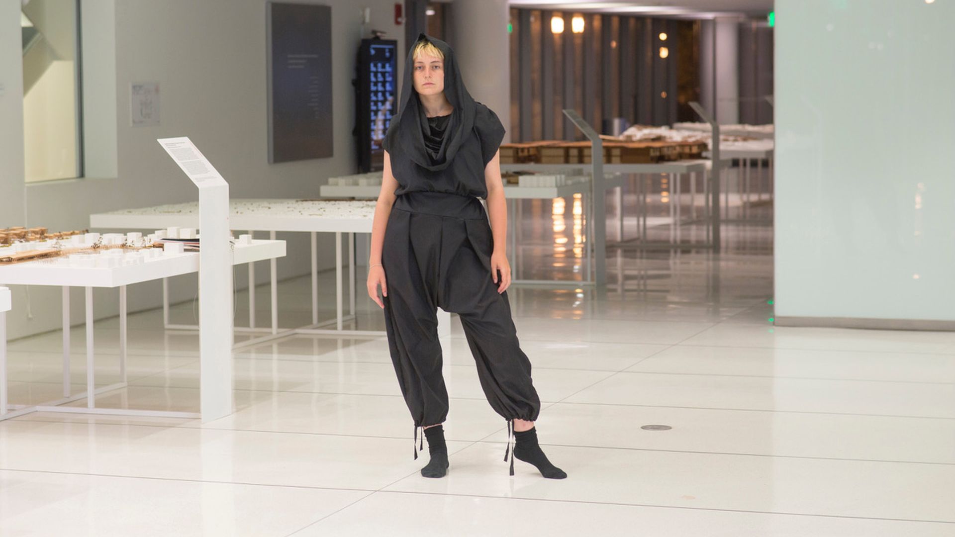 A woman poses in a loose black jumpsuit with a hood