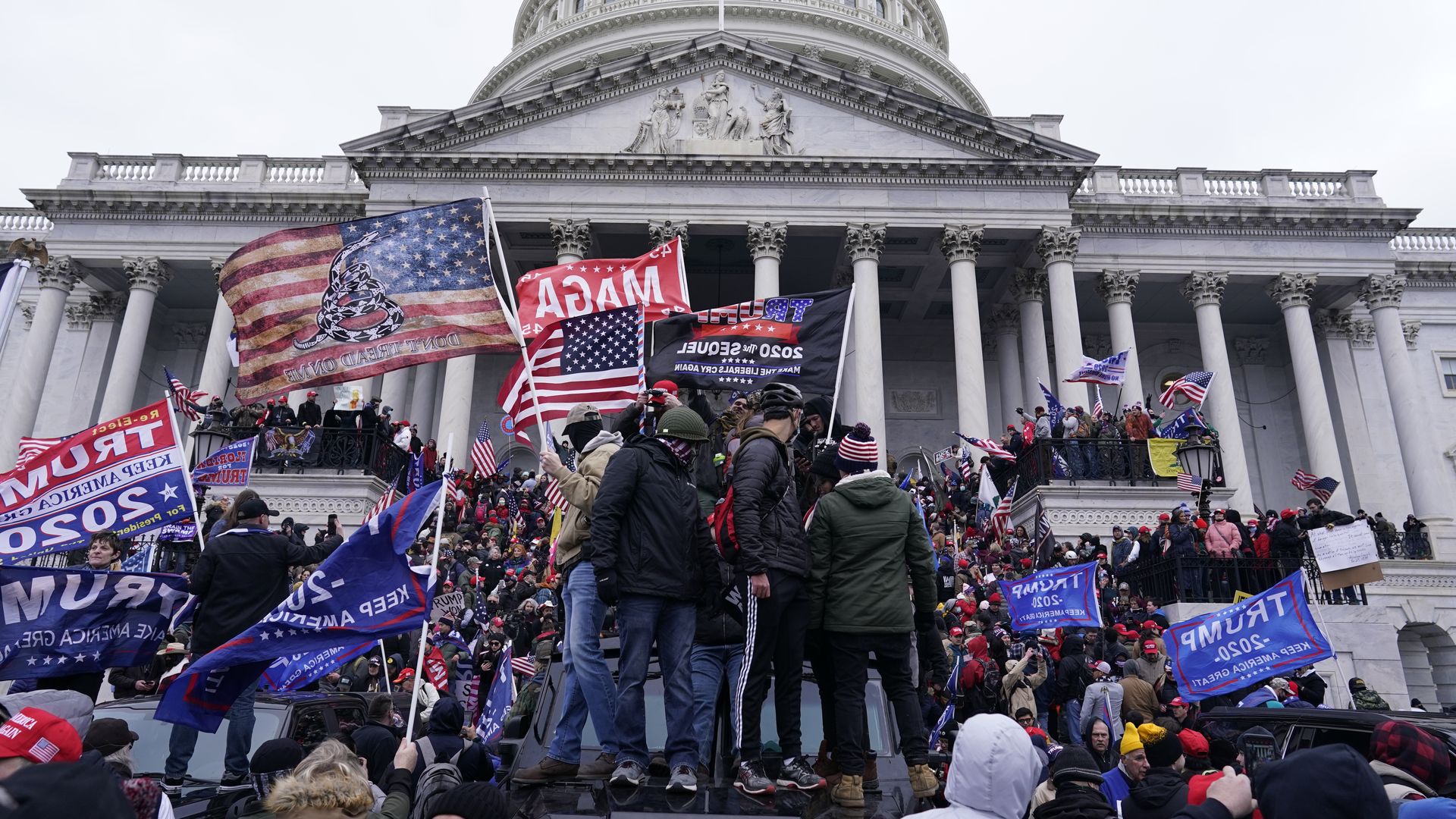 Pro-Trump rioters holding flags and wearing jackets storm the Capitol on Jan. 6. 
