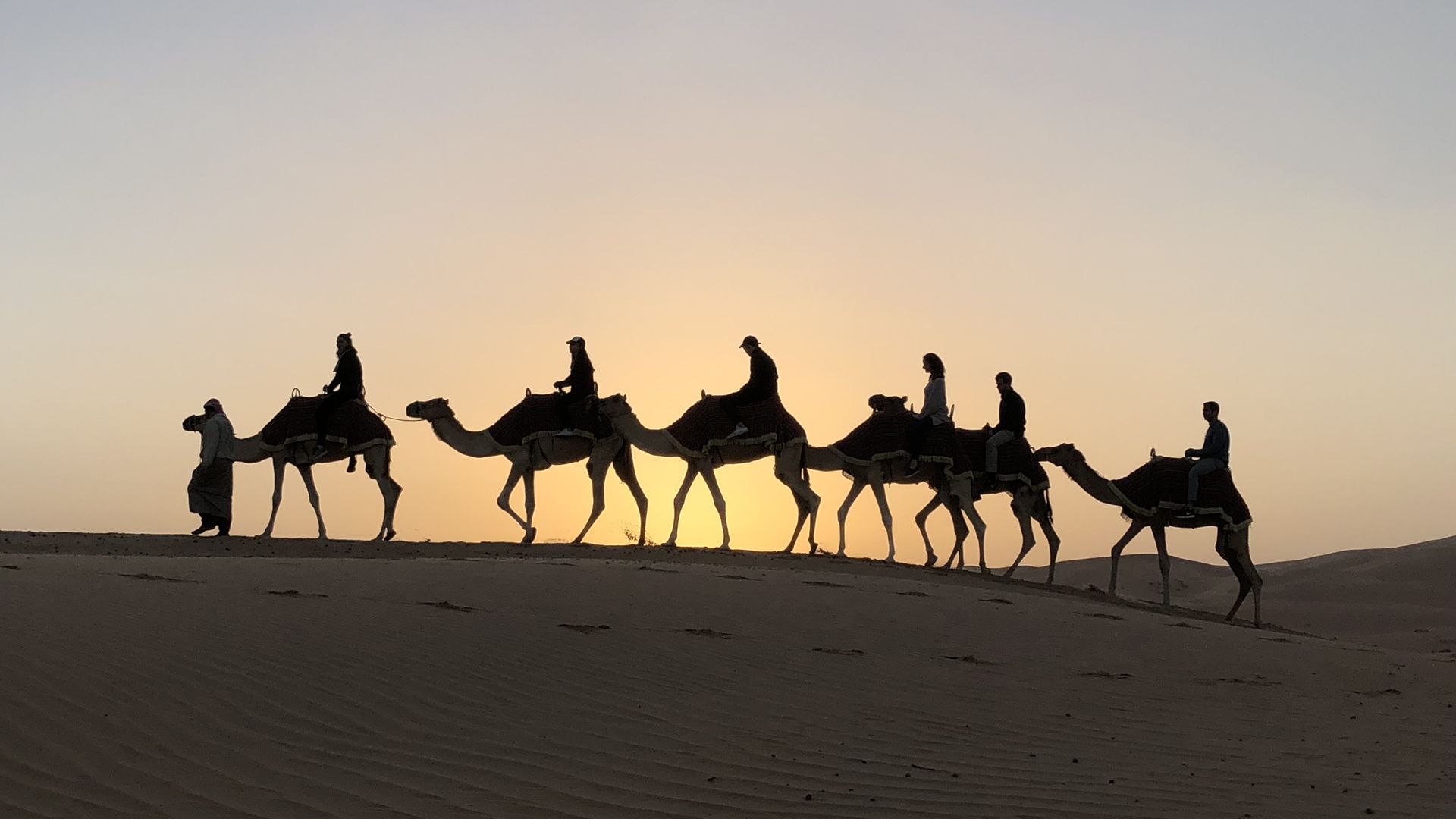 camel riders on ridge of sand dune
