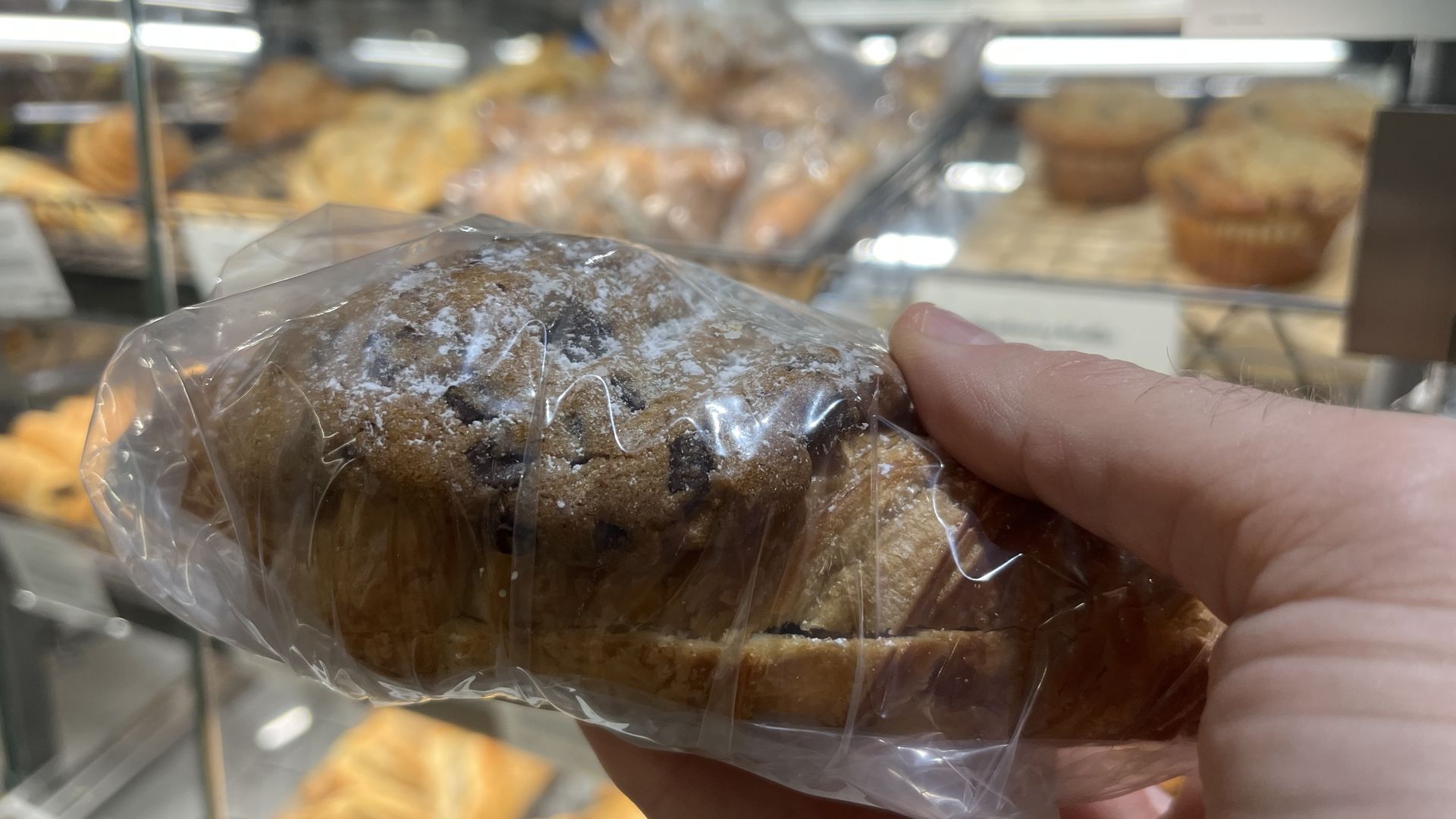 A person holding a cookie-croissant combo in a wrapping.