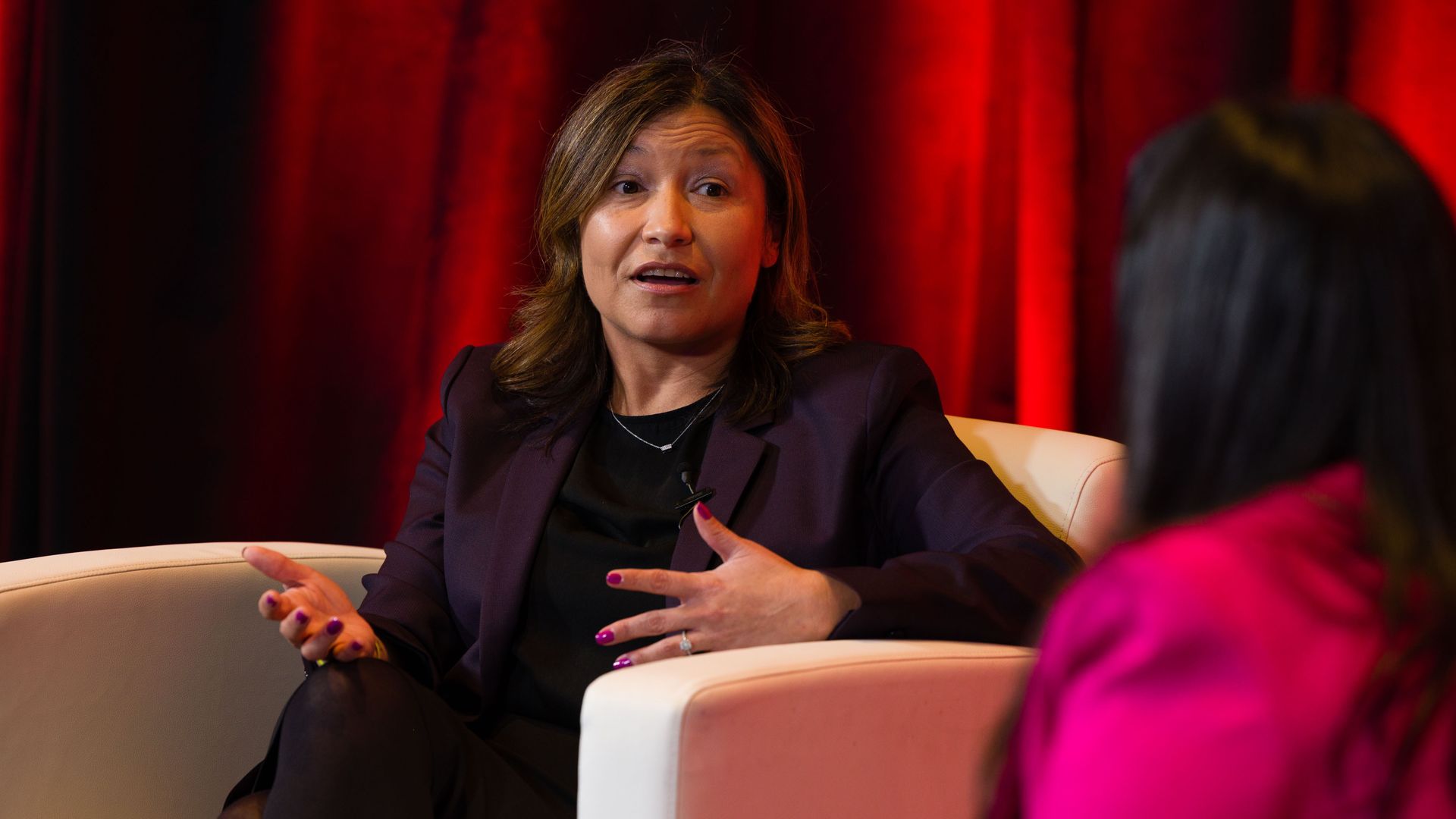 Julie Chávez Rodríguez sits in a chair and talks.