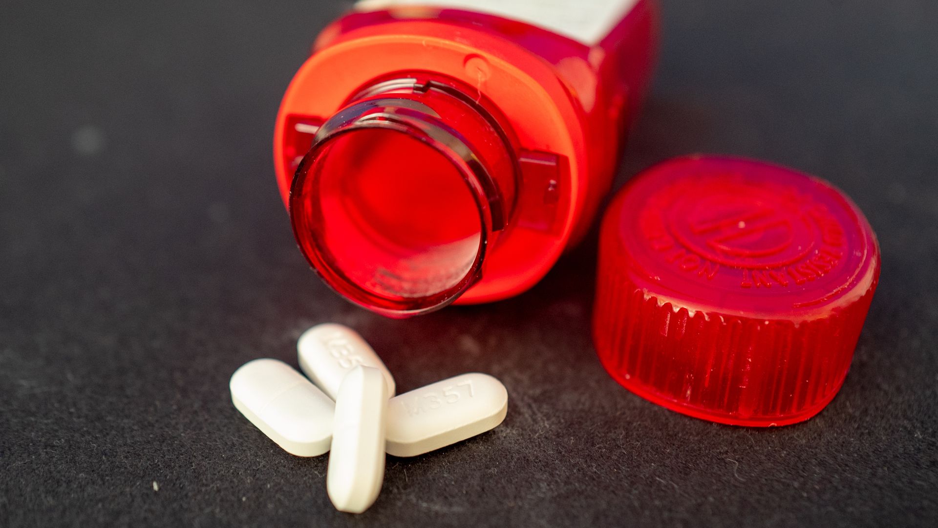 Picture of an opened pill bottle with opioid pills out of it