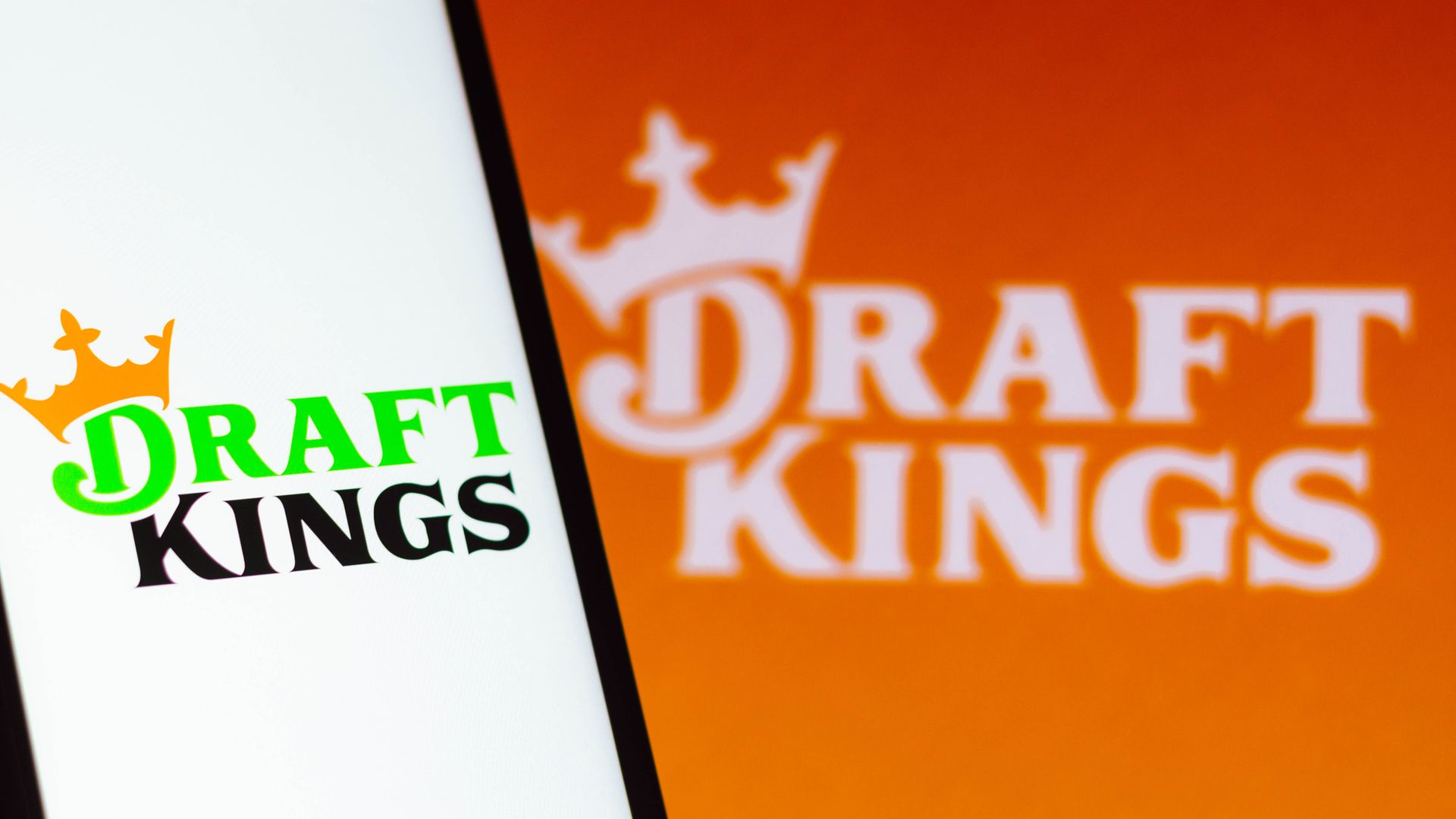 A phone displaying the "DraftKings" logo on its screen against an orange background that also displays the logo. 