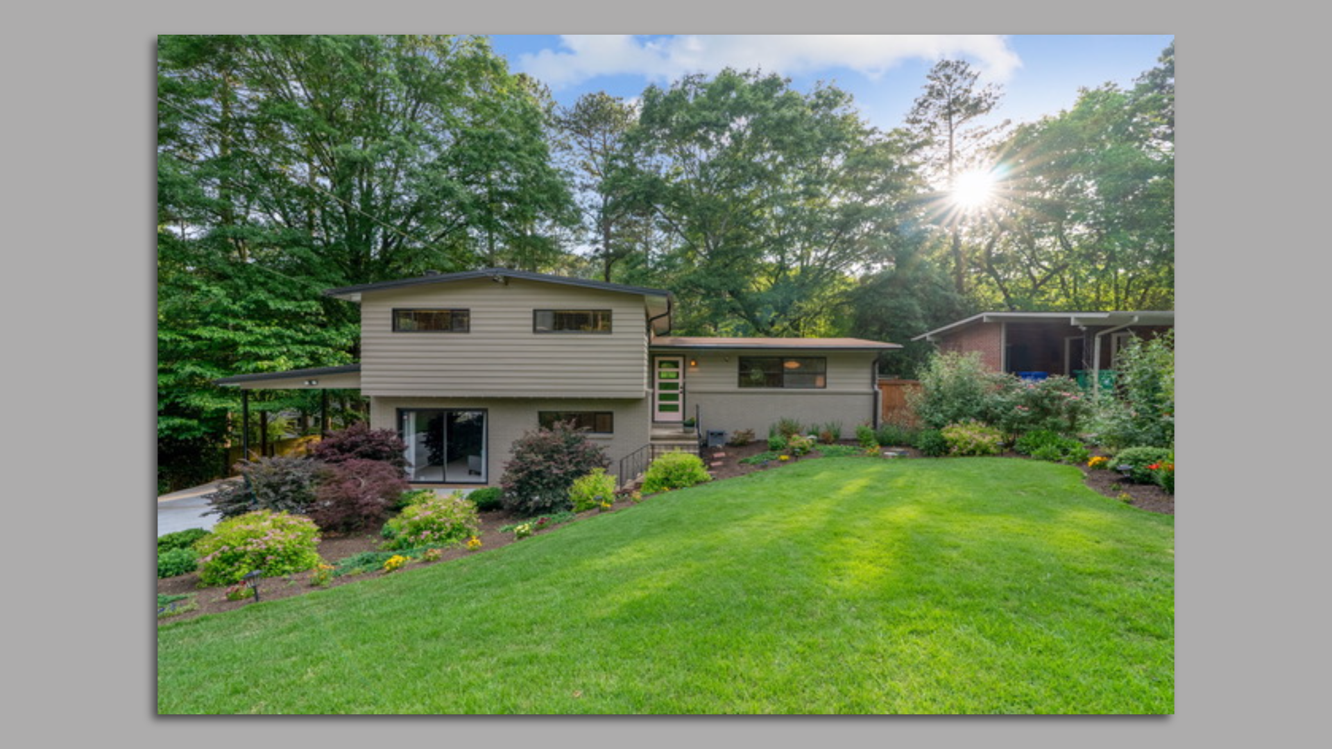A photo of a renovated mid-century modern split level home with a large sloped green grassy yard