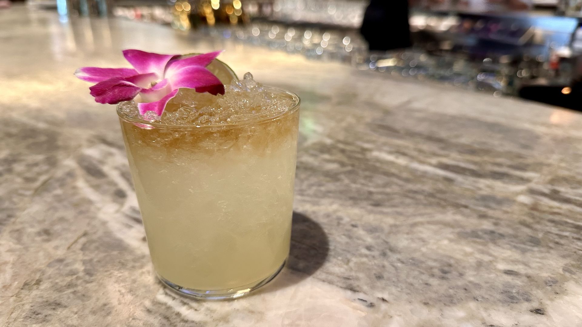 A light brown cocktail drink with a pink flower on the top left