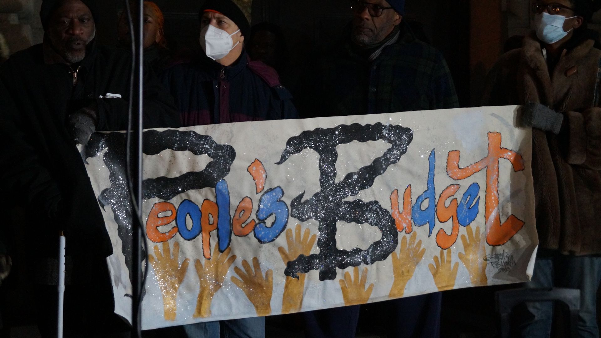 Activists wearing masks hold a "People's Budget" handmade sign. 