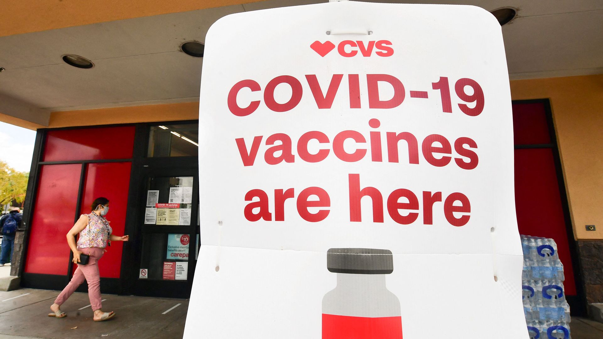 A white sign with red font outside a CVS pharmacy that says, "COVID-19 vaccines are here."