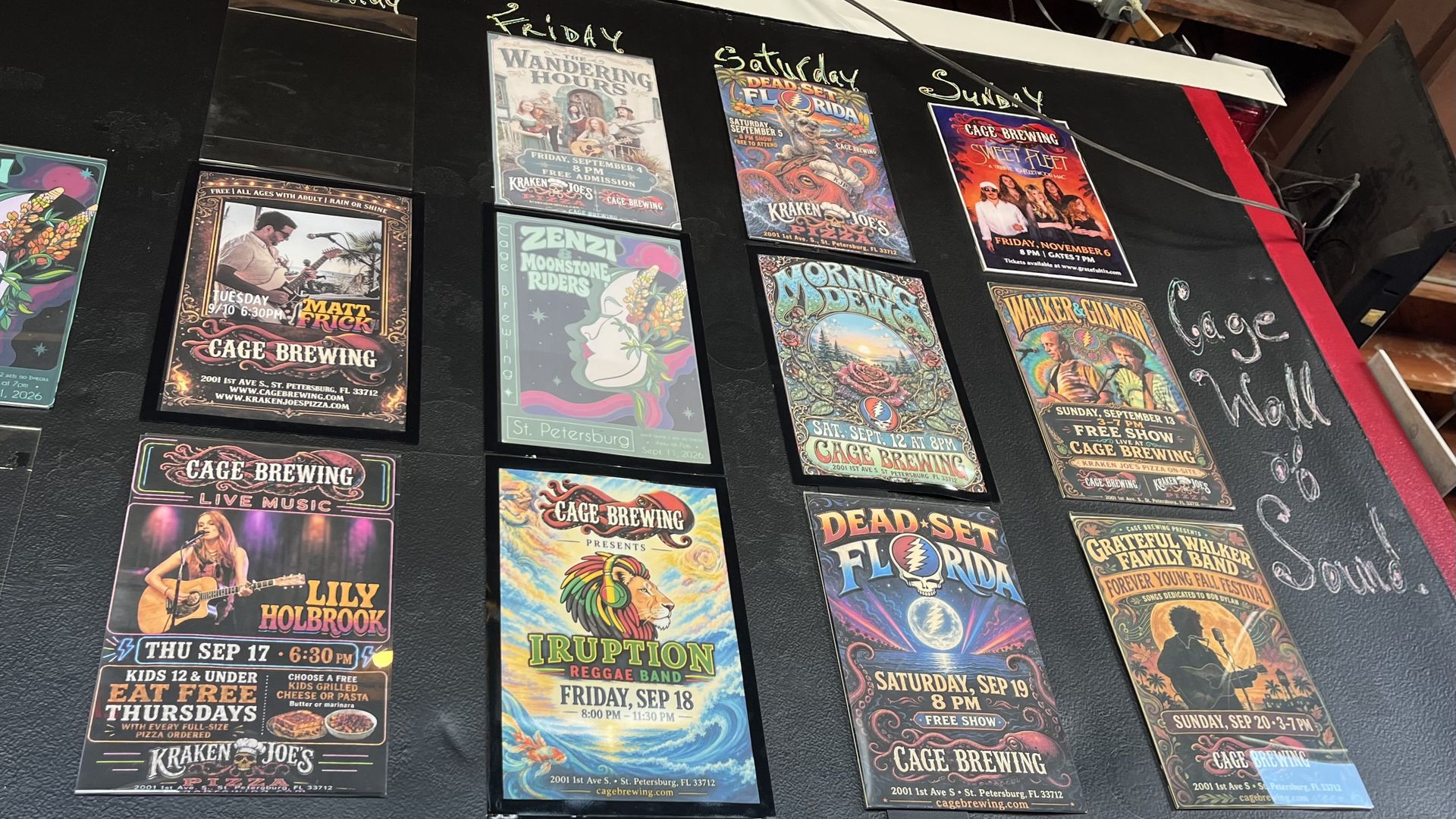 Black wall lined with colorful concert posters for Cage Brewing, arranged in a grid; includes band art, musician photos, and psychedelic graphics with weekday headings above.