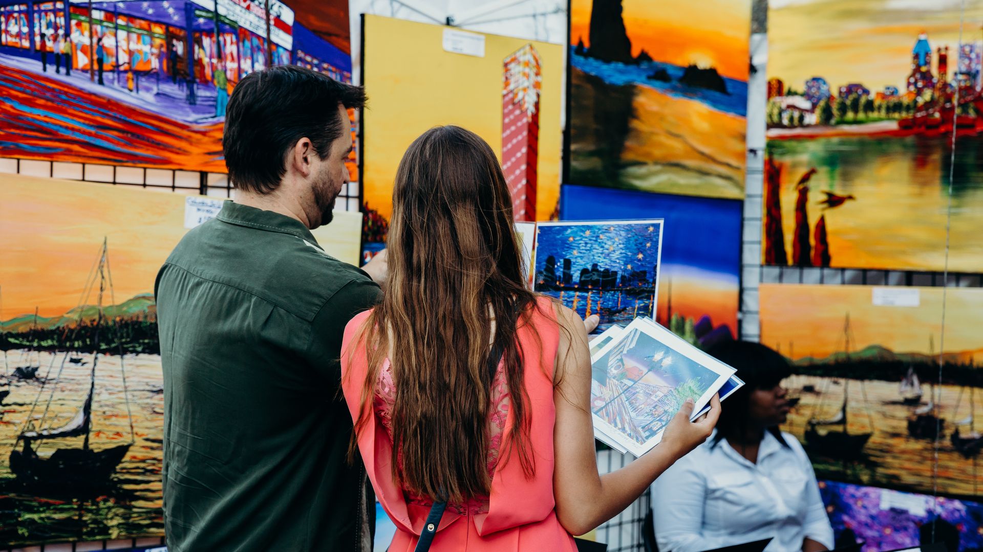 A man and a woman look at colorful prints at the NW 13th Ave outdoor art market in Portland's Pearl District.