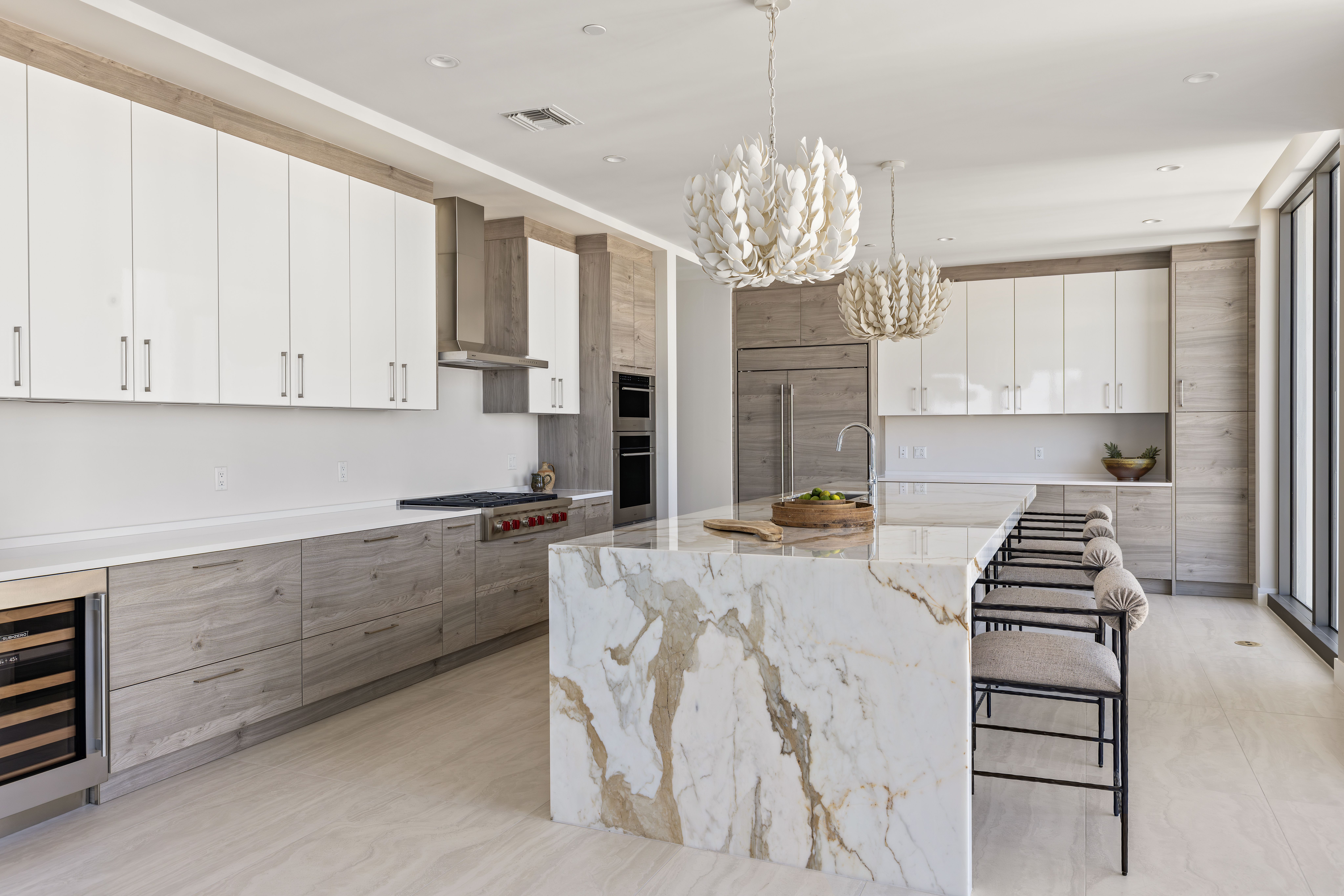 A kitchen with white and sand-colored cabinets and a giant marble island of the same colors.