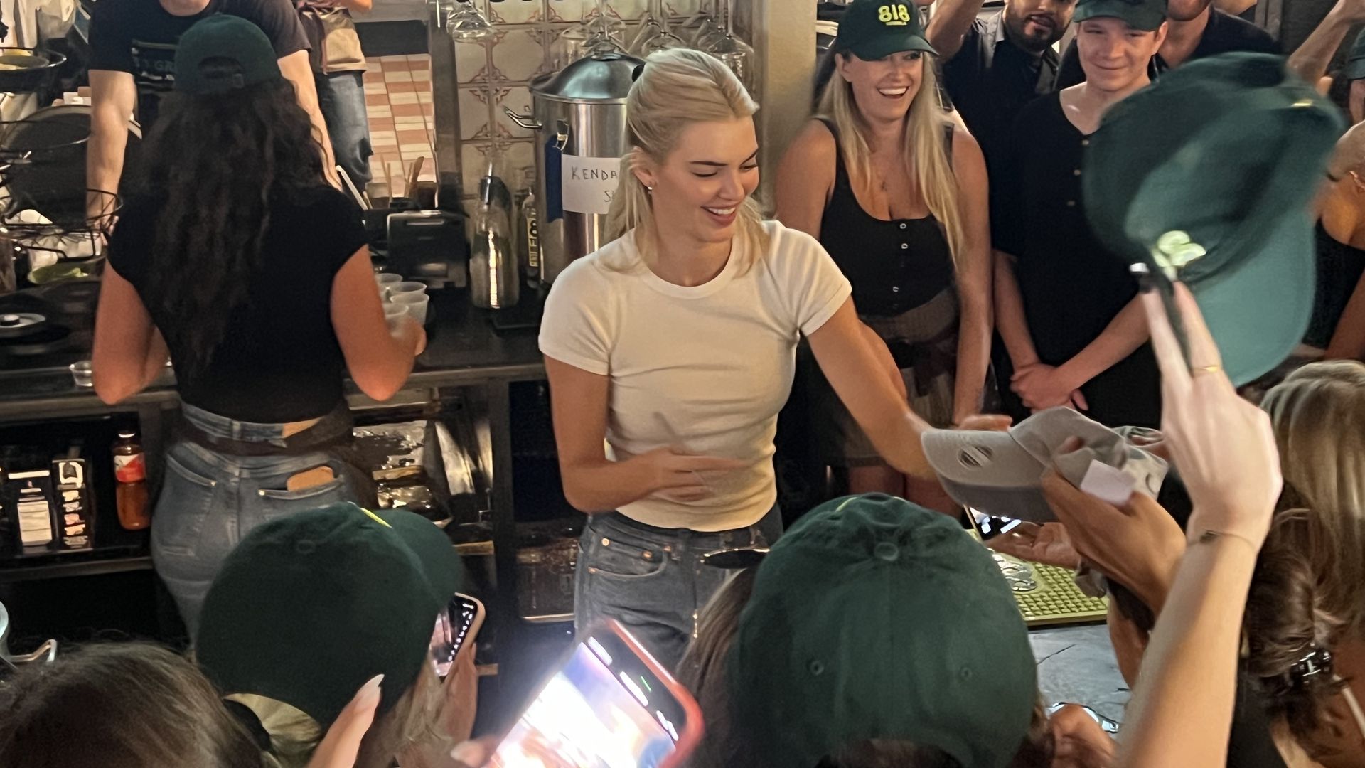 A woman in a white shirt hands out a hat inside a crowded bar. 
