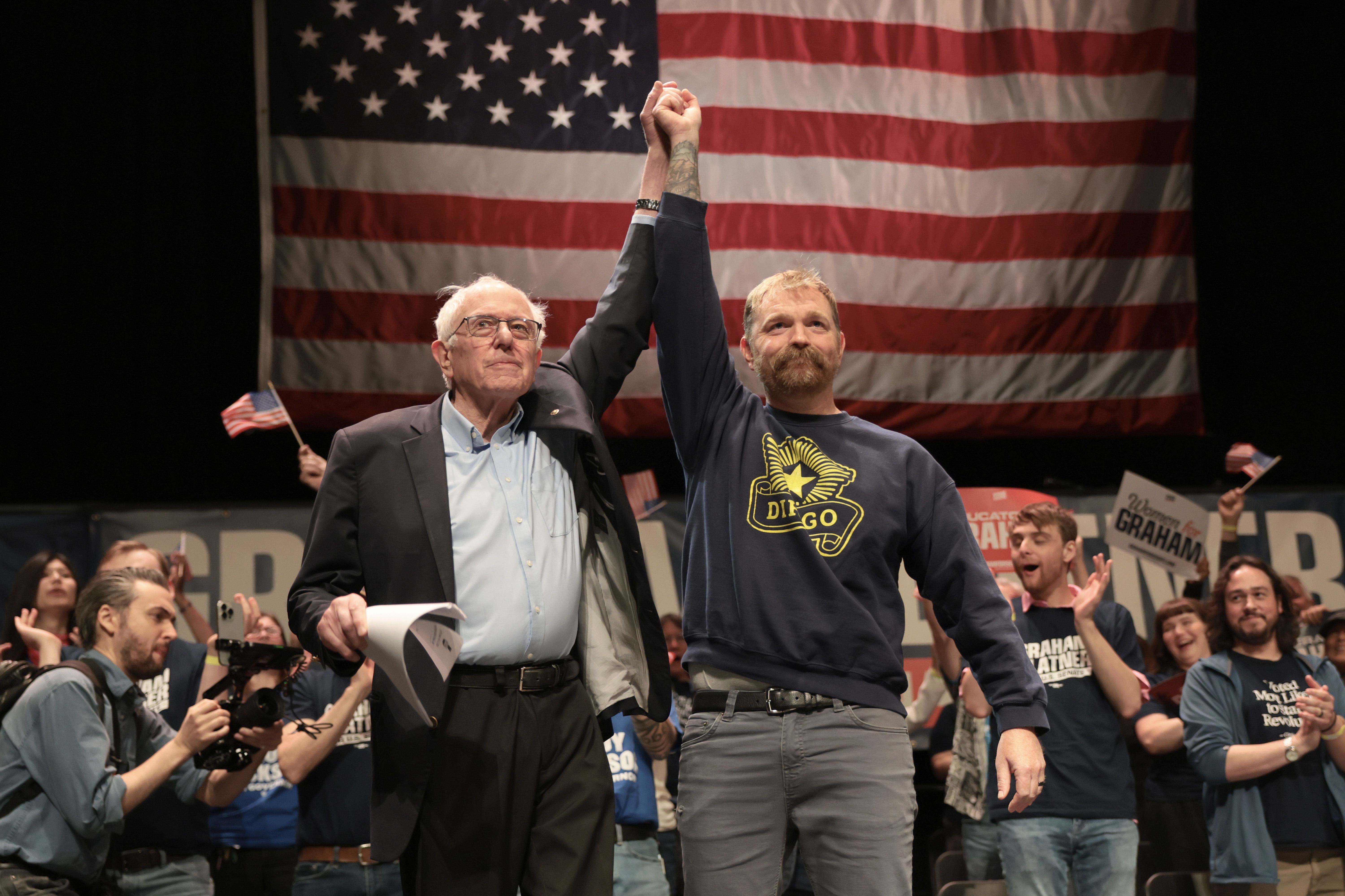 Bernie Sanders and Graham Platner hold up their interlocked hands together at a rally