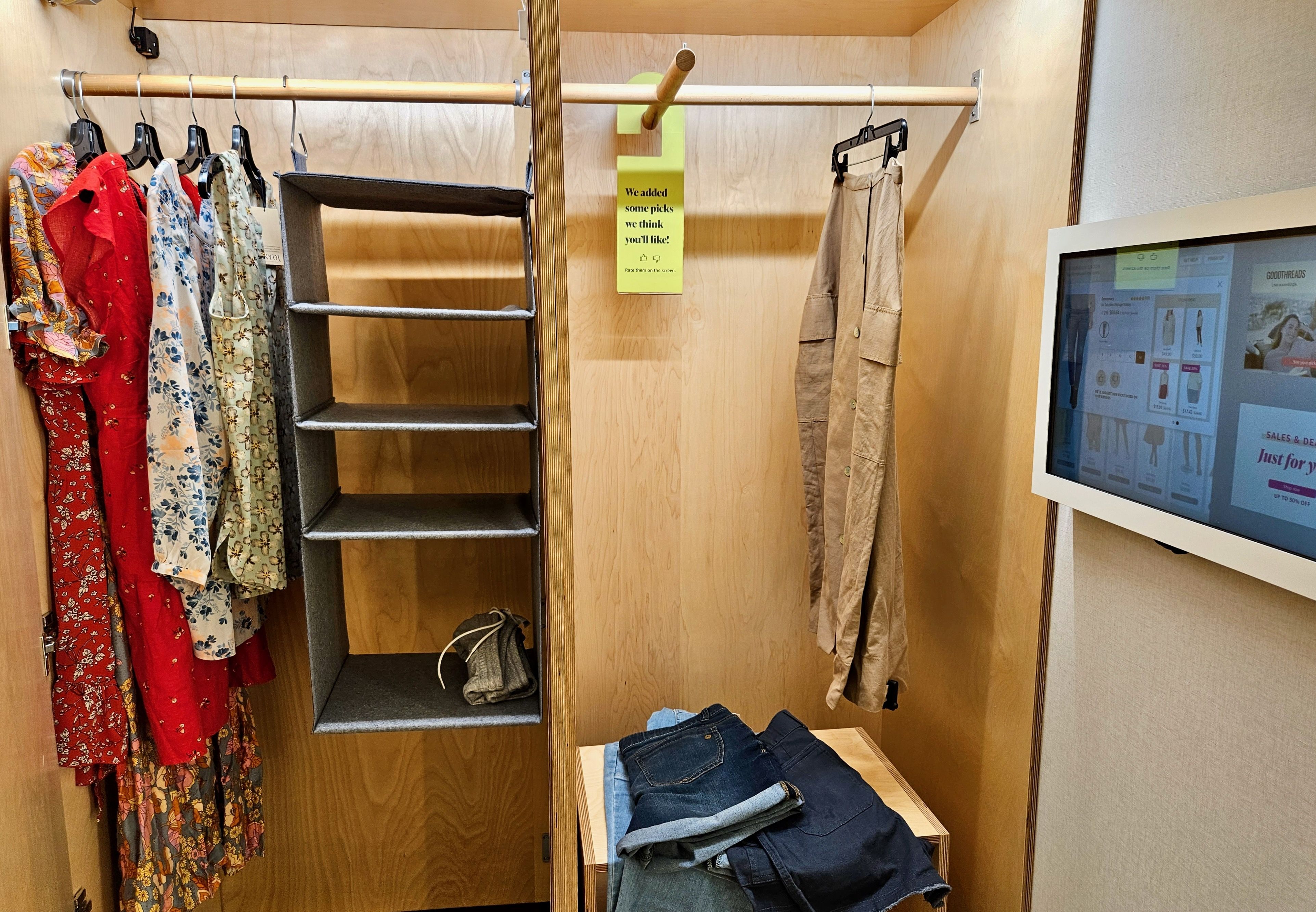 A closet with dresses and jeans inside, next to a touch screen on the right wall
