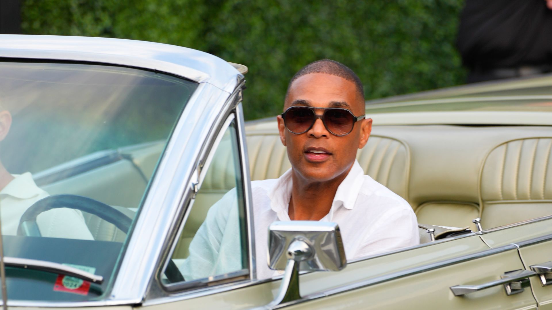 Don Lemon, wearing white, drives a convertible past the photographer.