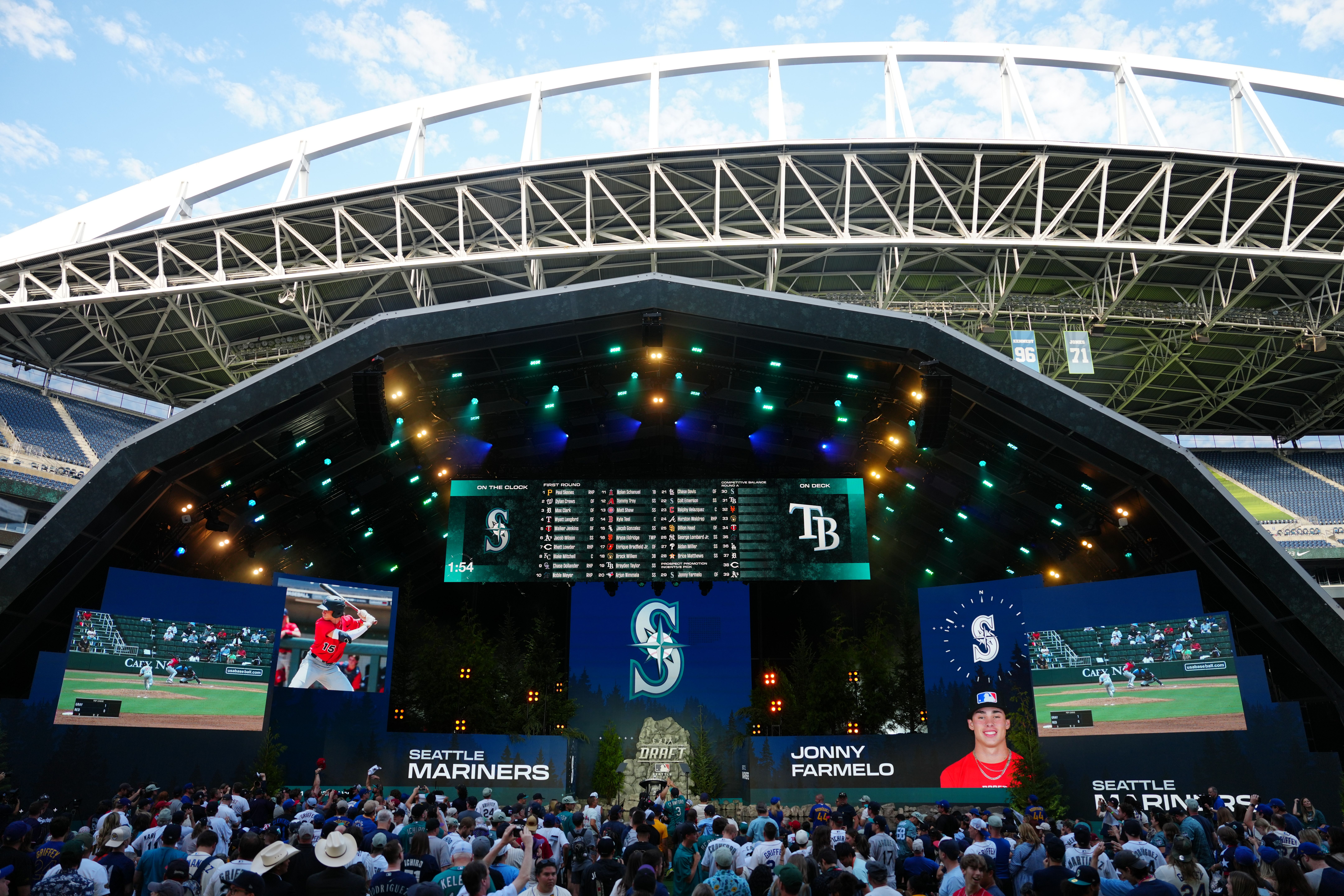 Lumen Field is shown lit up and with the Seattle Mariners logo as a crowd looks on at screens.