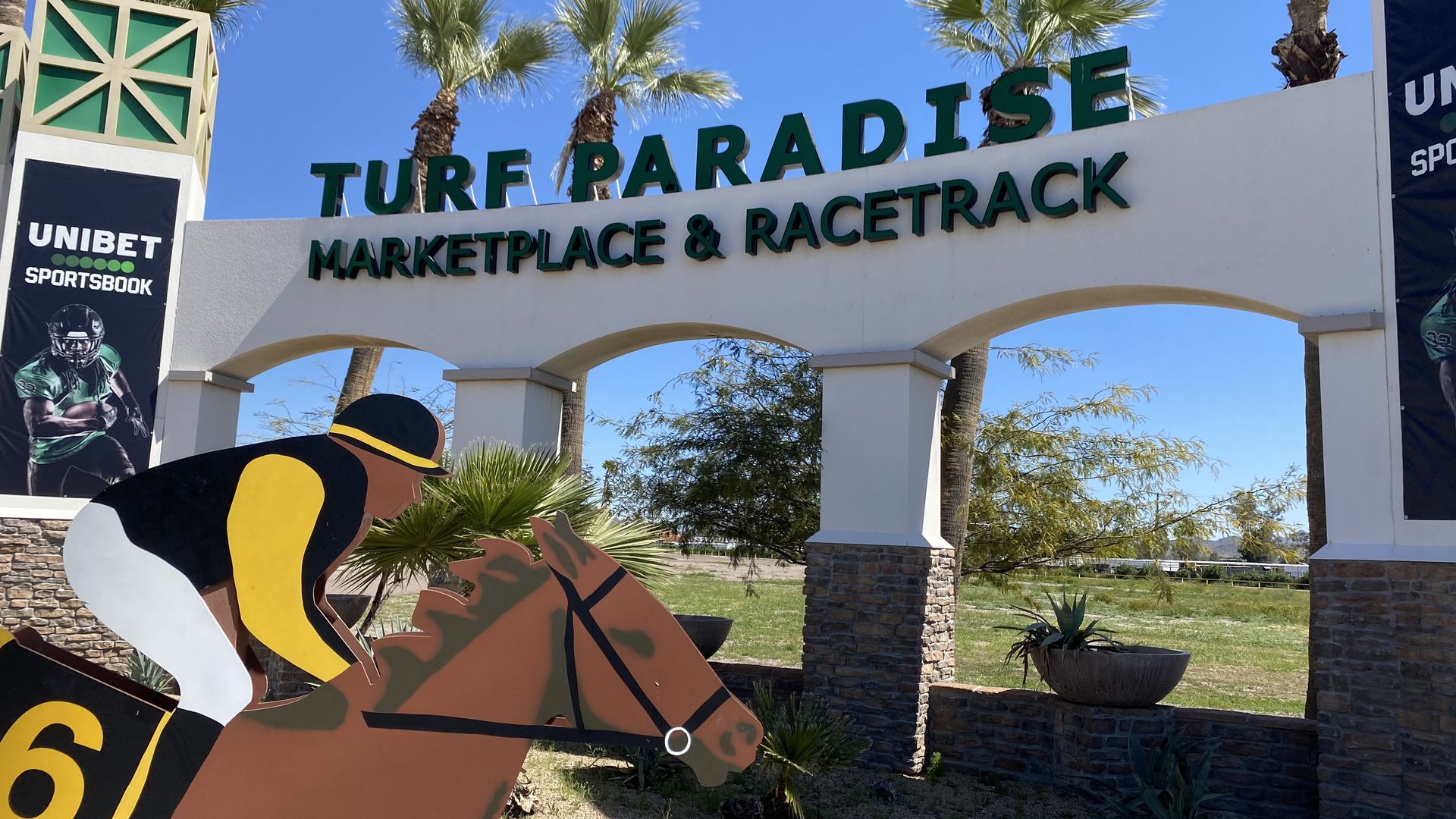 A two dimensional statue of a jockey on a horse under a sign that says Turf Paradise. 