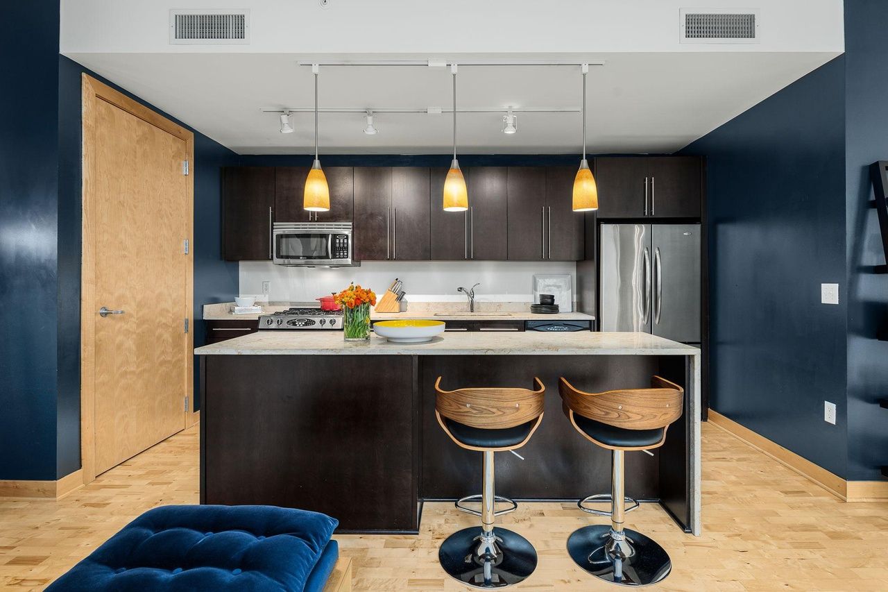 A kitchen with dark blue walls and black cabinets. There is a kitchen island in the middle.