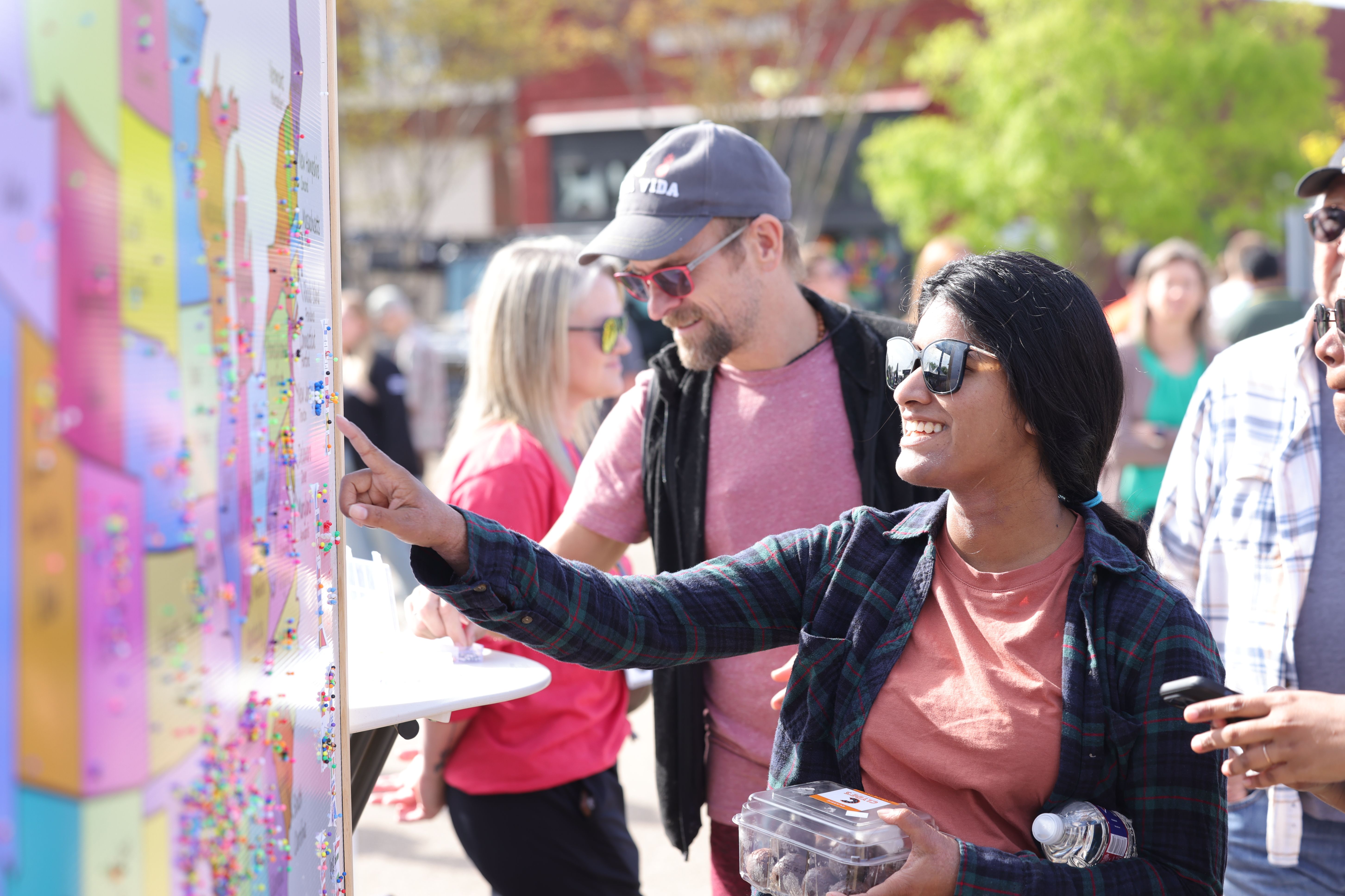 People look and point at a map of the U.S. marked with pins. 